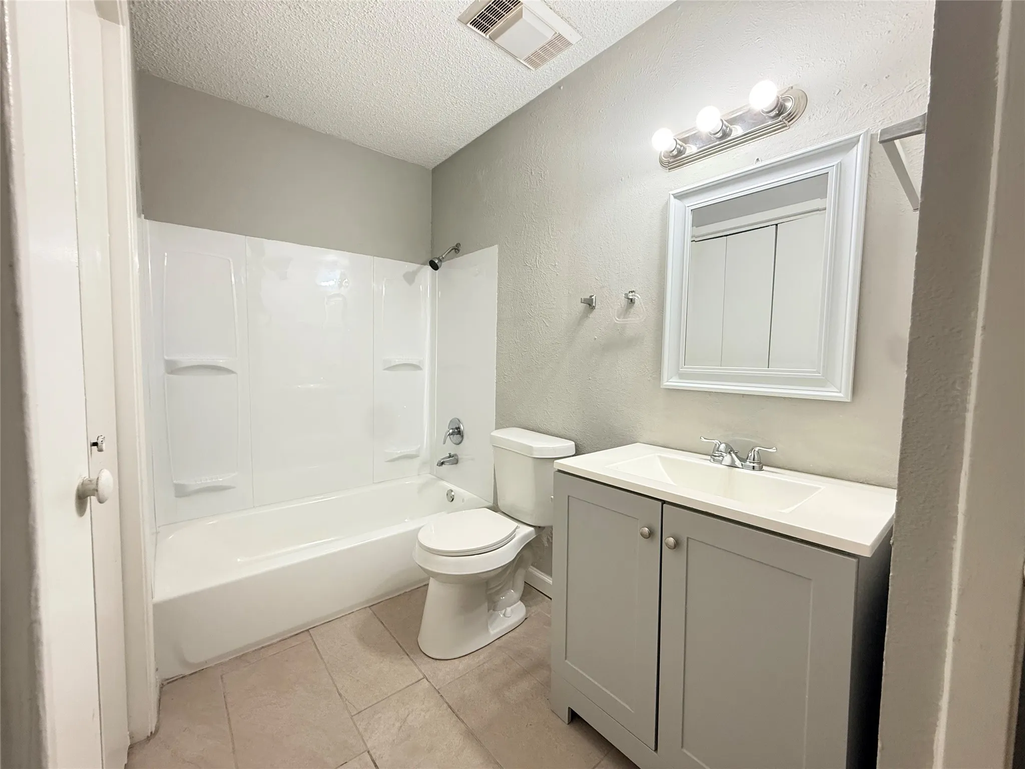 Bathroom featuring a white bathtub with a shower surround, a white toilet, and a vanity with a gray base cabinet and an integrated white sink