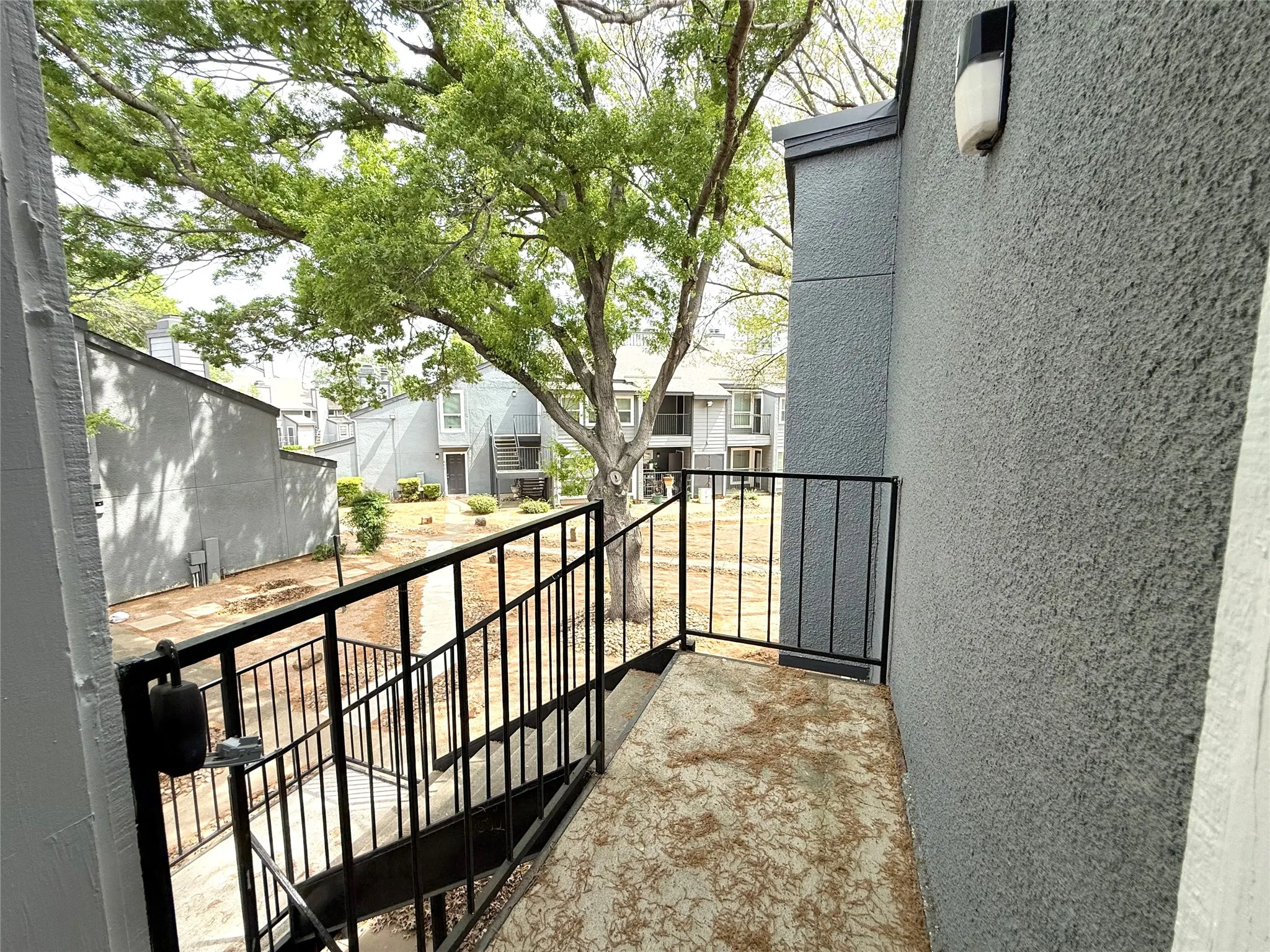 Outdoor balcony with black metal railings, textured gray exterior wall, and an exterior light fixture