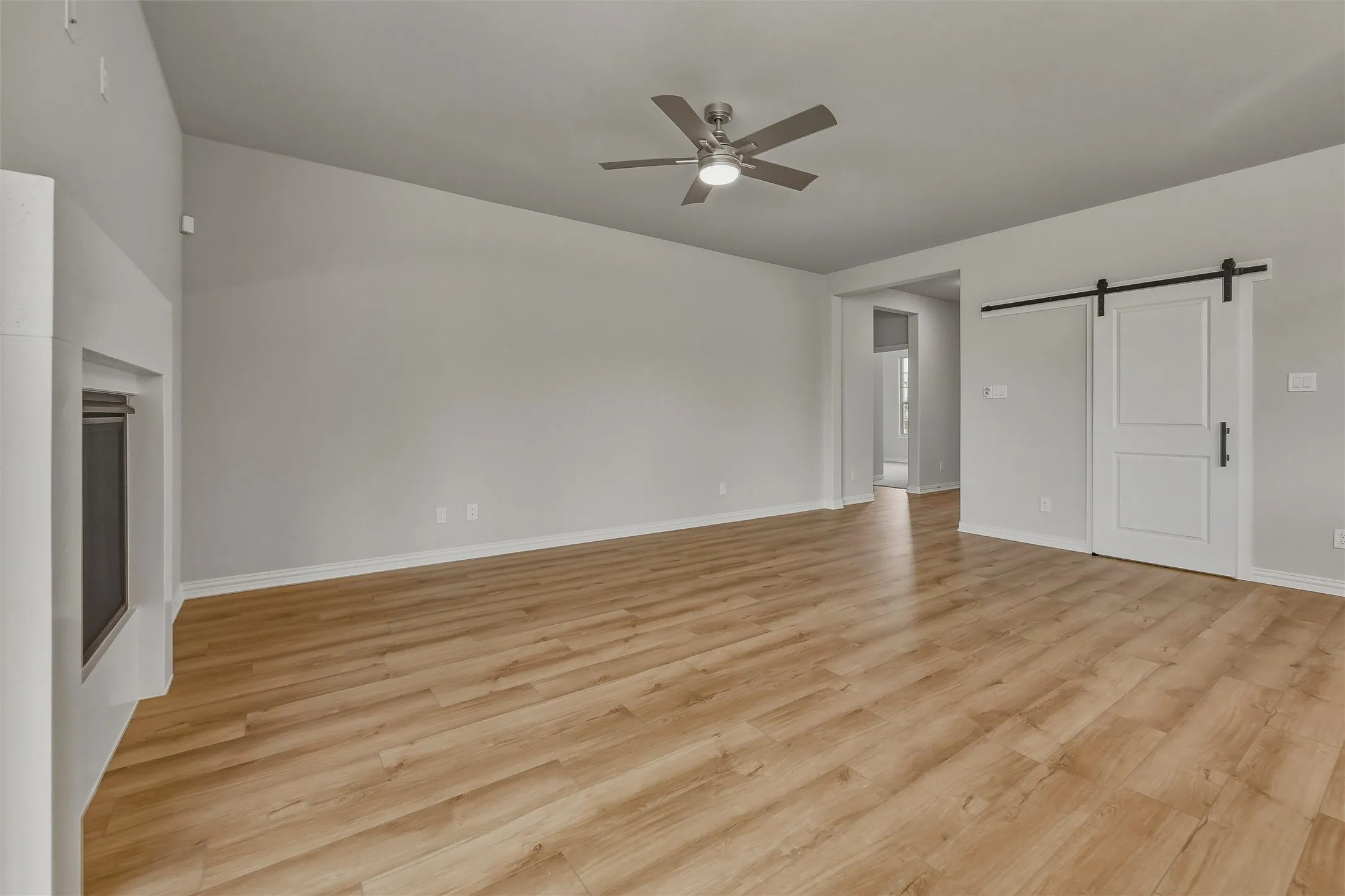 Wood-finish flooring, recessed fireplace, white barn door, modern ceiling fan, and vaulted ceiling