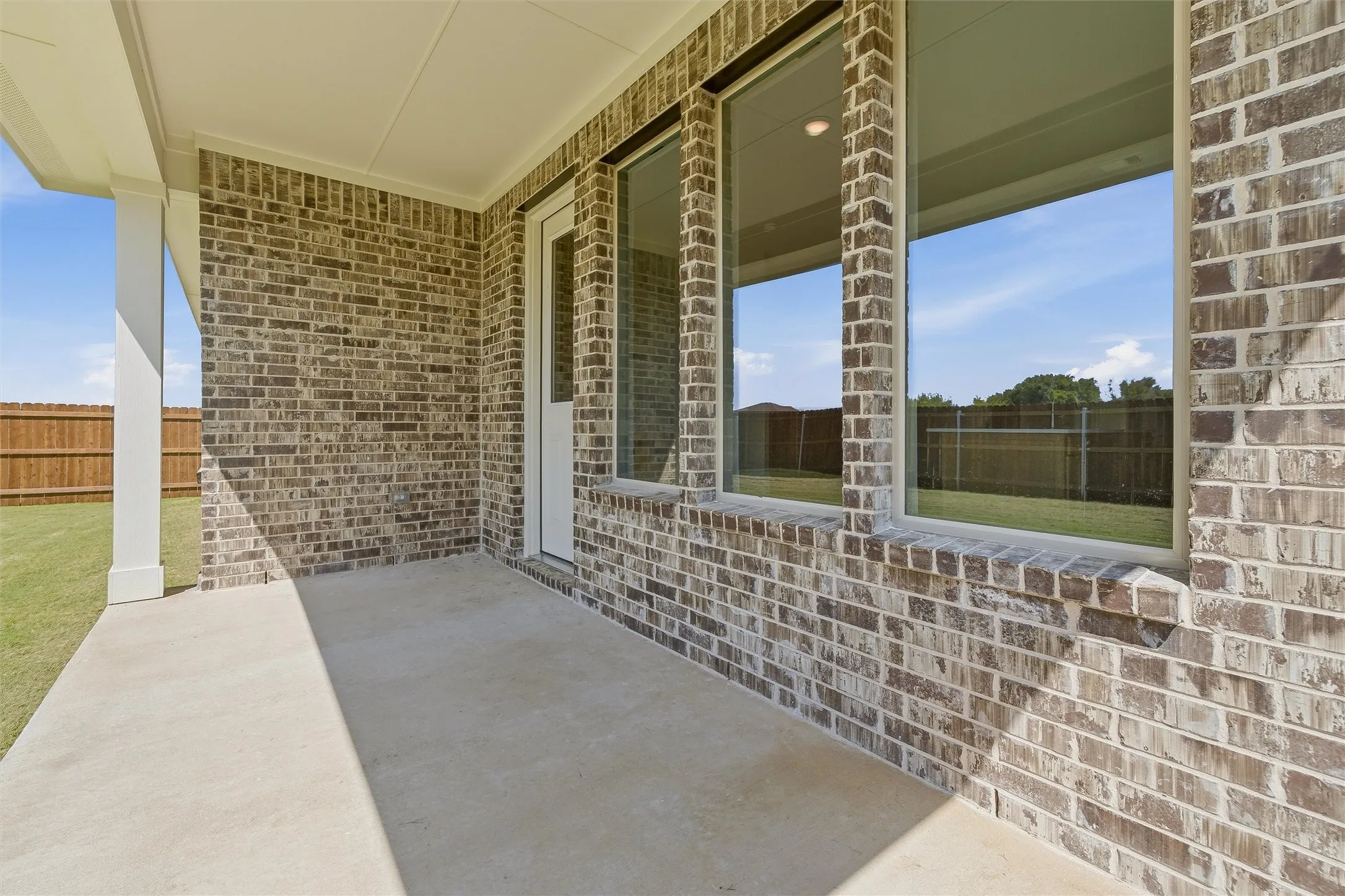 Covered patio with a concrete surface, brick exterior, and a white support column