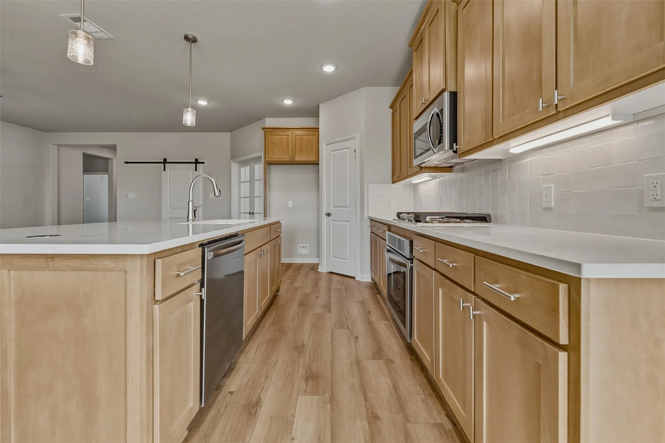 Kitchen featuring wood-finish flooring, light wood cabinetry, white countertops, stainless steel appliances, and a tile backsplash