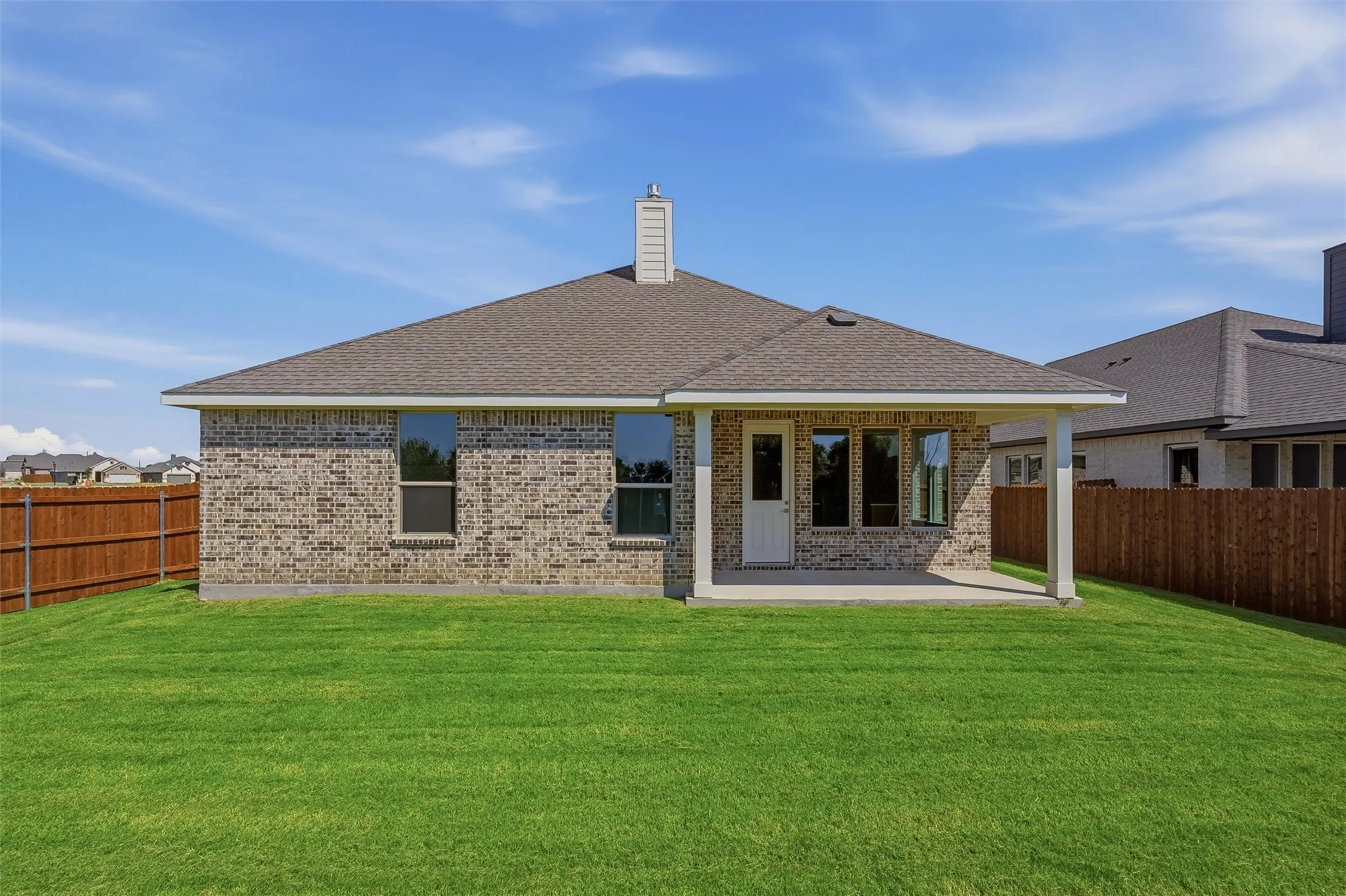 Expansive backyard with a manicured lawn, brick exterior, covered patio, and privacy fencing