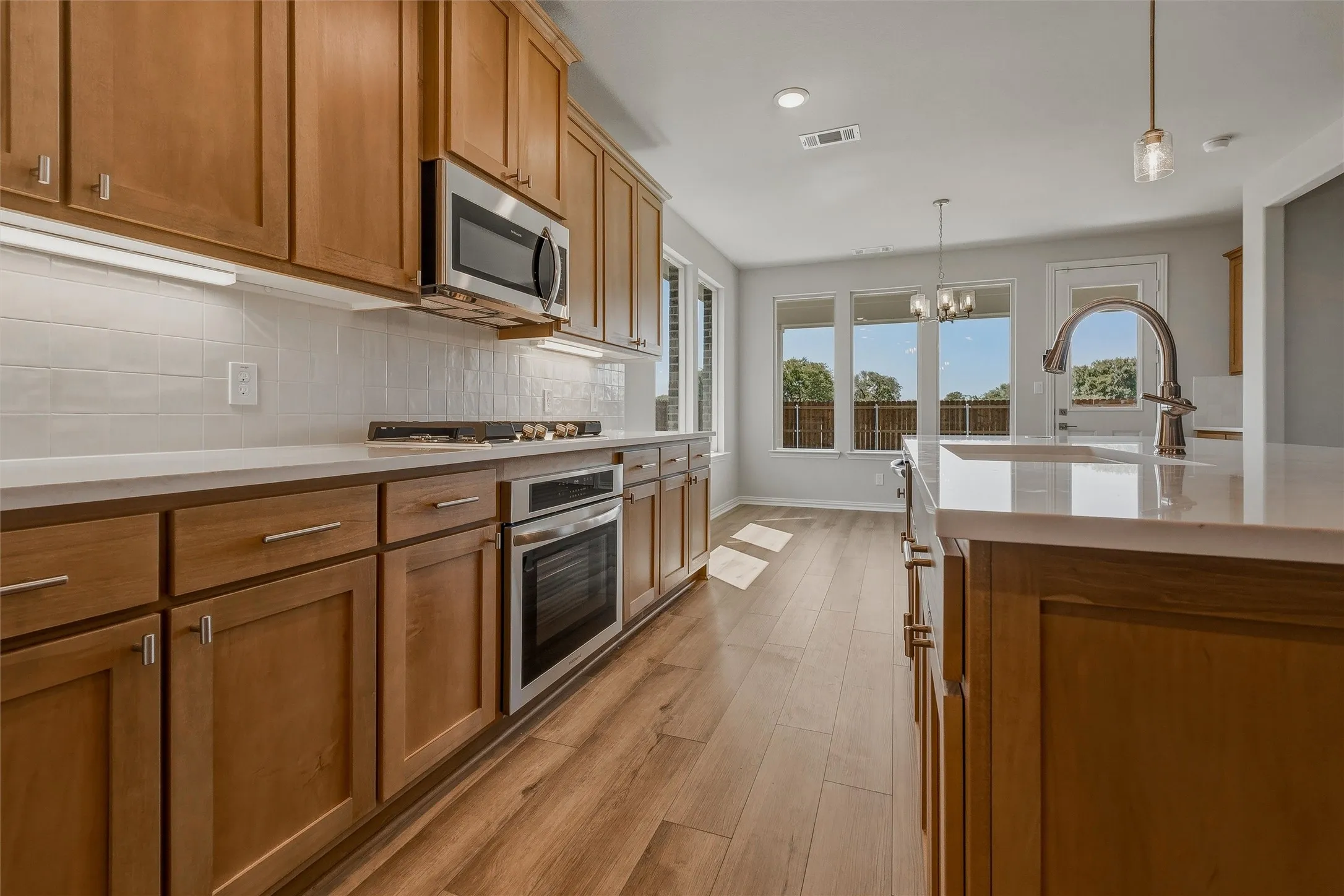 Wood-finish flooring throughout, wood cabinetry with brushed nickel hardware, stainless steel appliances, white subway tile backsplash, and light-toned countertops