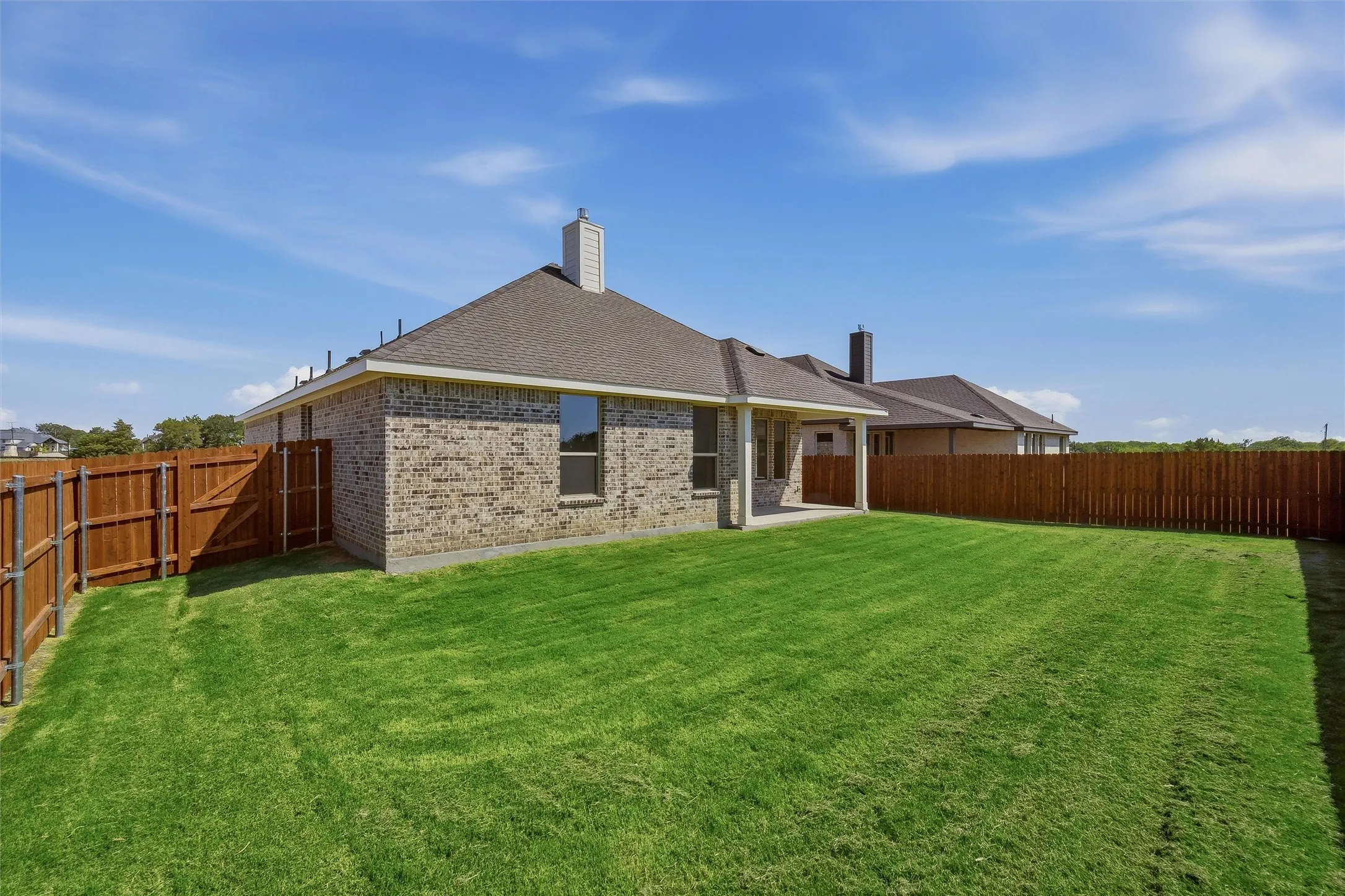 Expansive backyard featuring a new wood privacy fence, a covered concrete patio, and a brick exterior