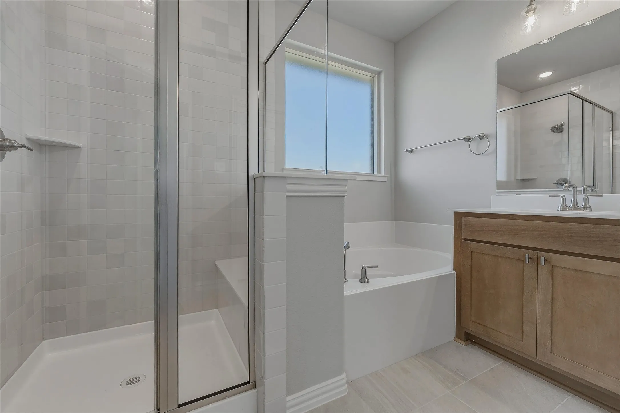 Glass-enclosed shower with tile surround and built-in bench, corner soaking tub, wood-finish vanity with countertop, and tile flooring