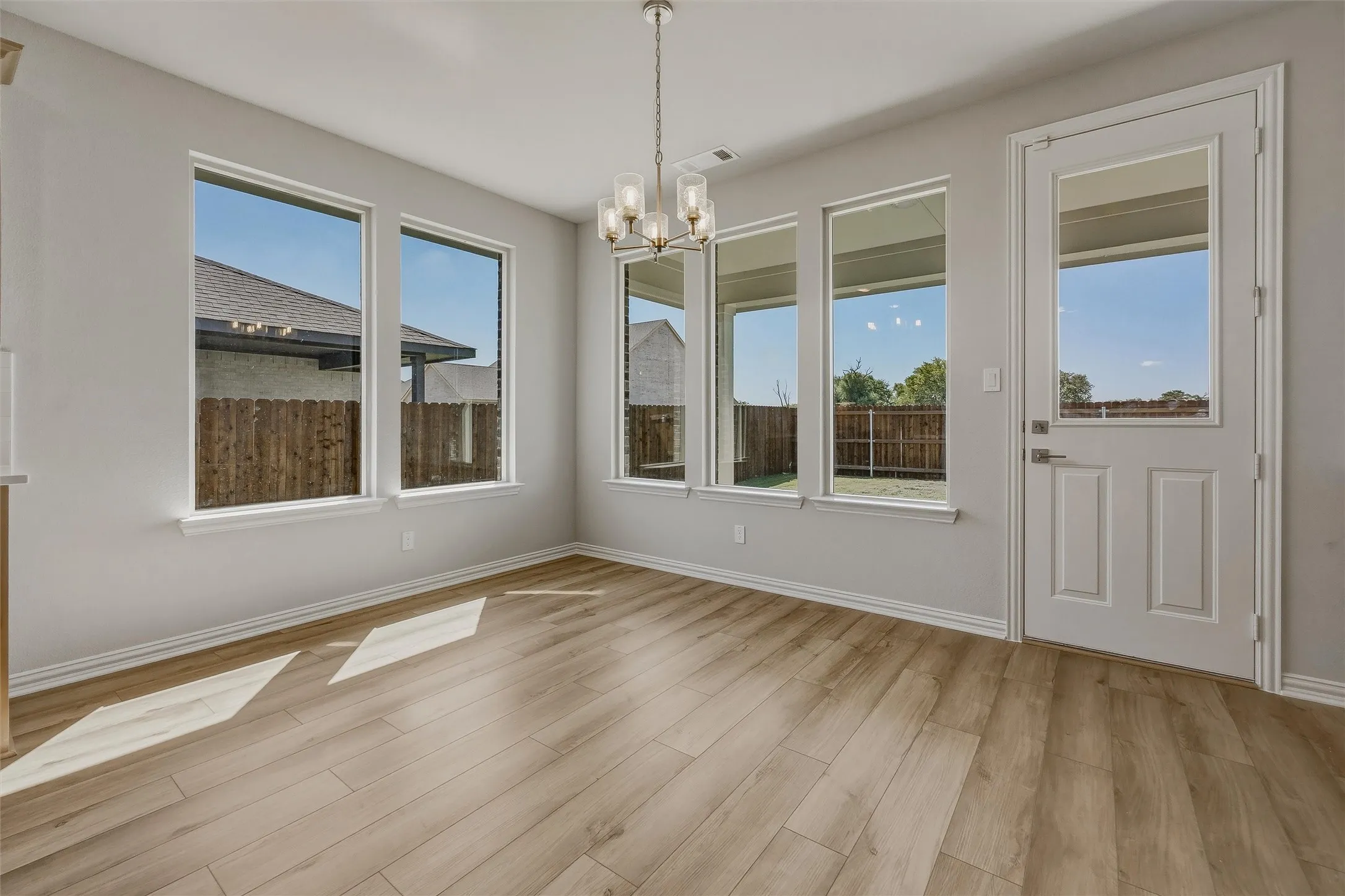 Wood-finish flooring with a modern multi-light chandelier, multiple large windows, and a panel door with a clear glass insert