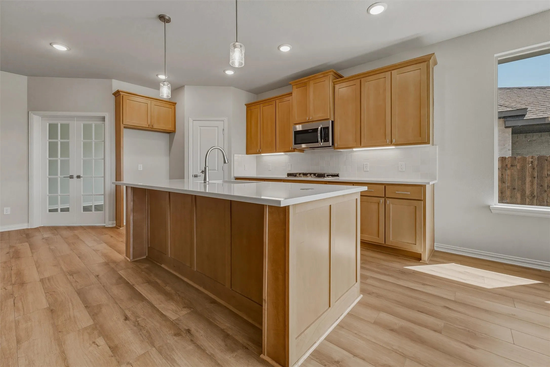 Expansive kitchen featuring wood-finish cabinetry, a large center island with a sink, stainless steel appliances, and a tile backsplash