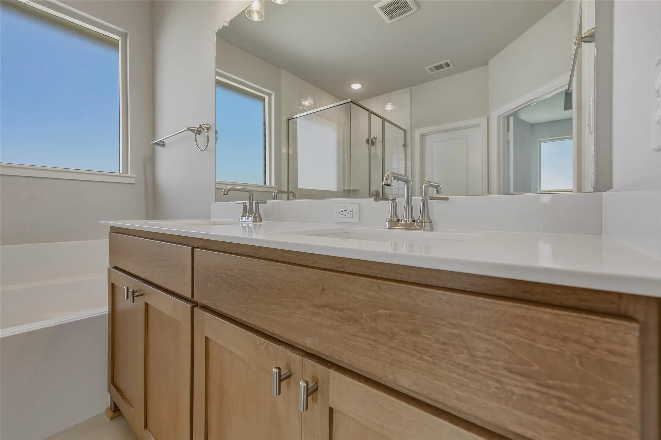Dual vanity with wood-finish cabinetry, integrated sinks, chrome fixtures, and a framed mirror