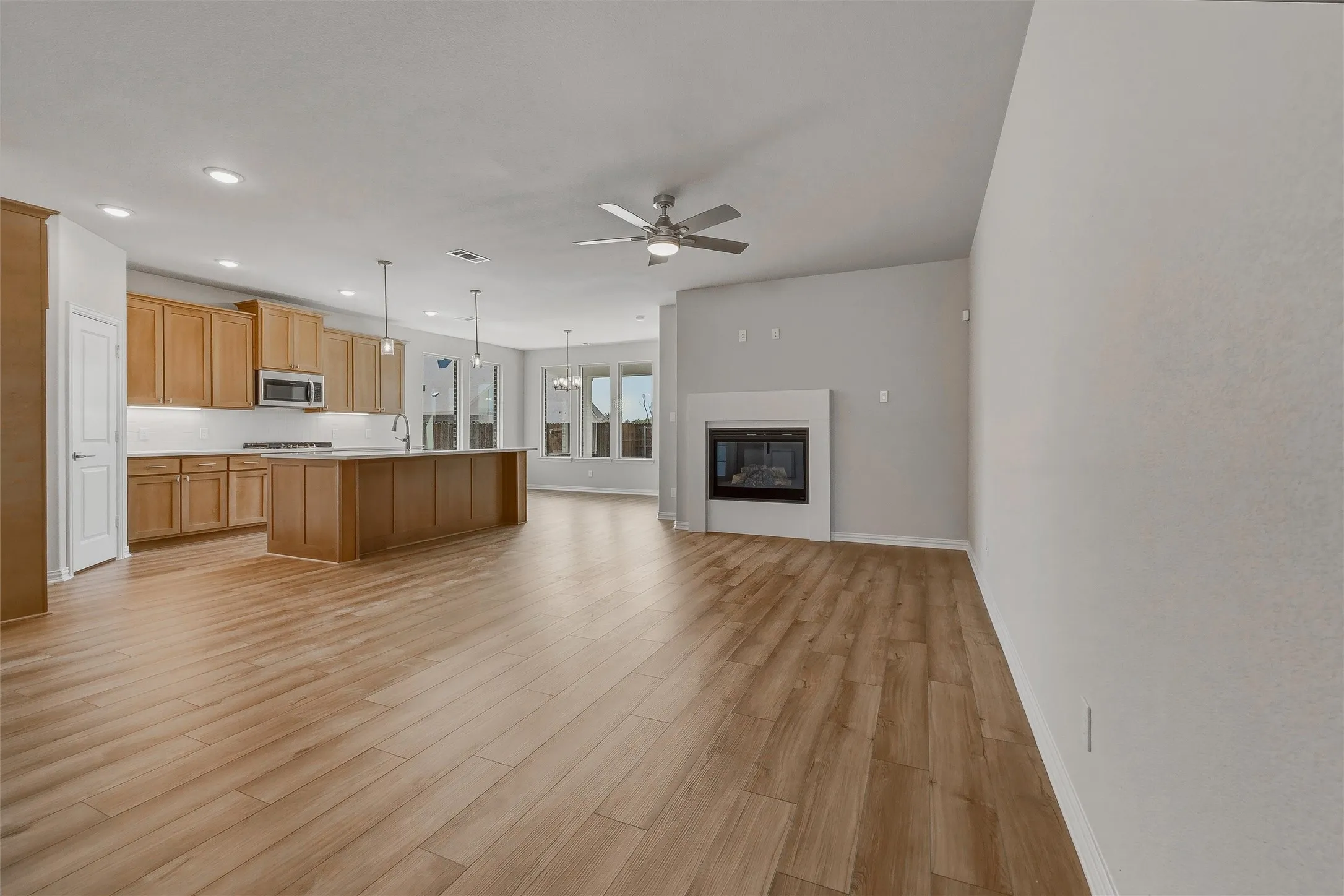 Wood-finish flooring throughout, kitchen with light wood cabinetry, built-in microwave, and pendant lighting