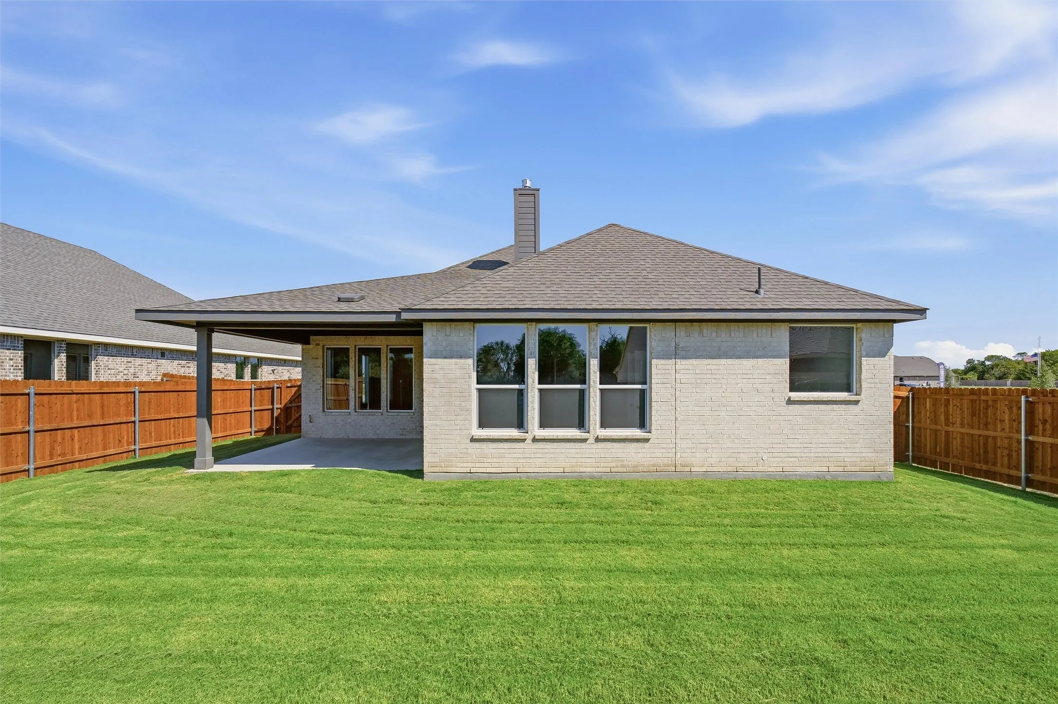 Expansive backyard featuring a covered patio, neutral brick exterior, and a wood privacy fence