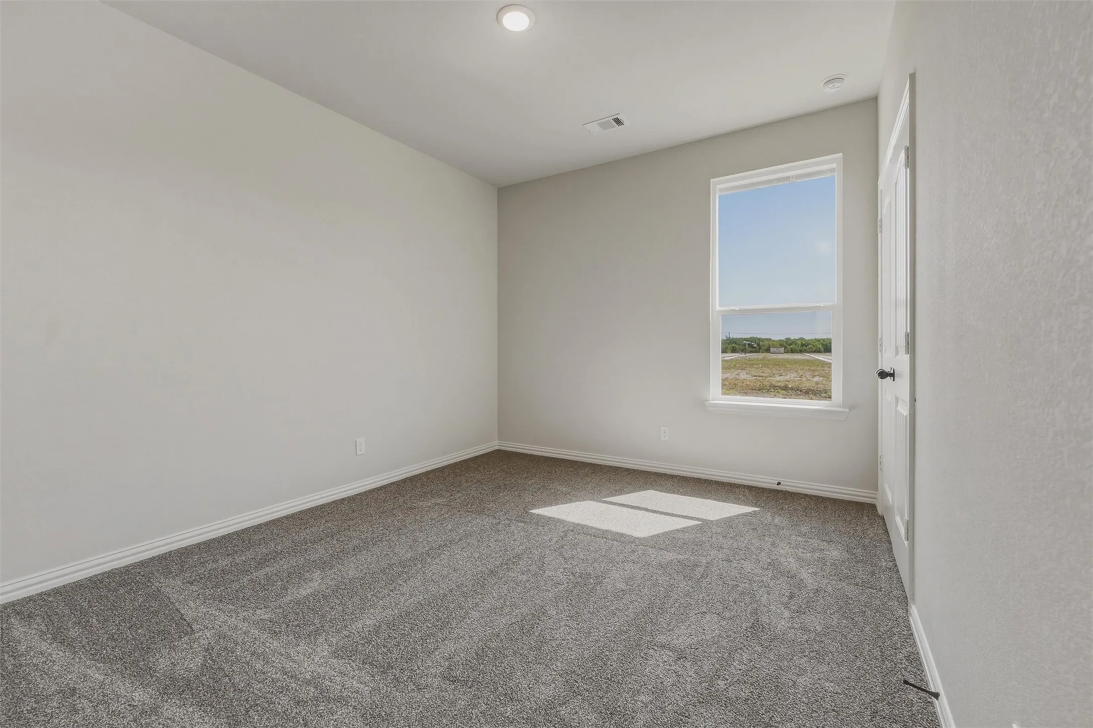 Neutral tone walls, recessed lighting, gray carpeting, single window, and a paneled door with dark hardware