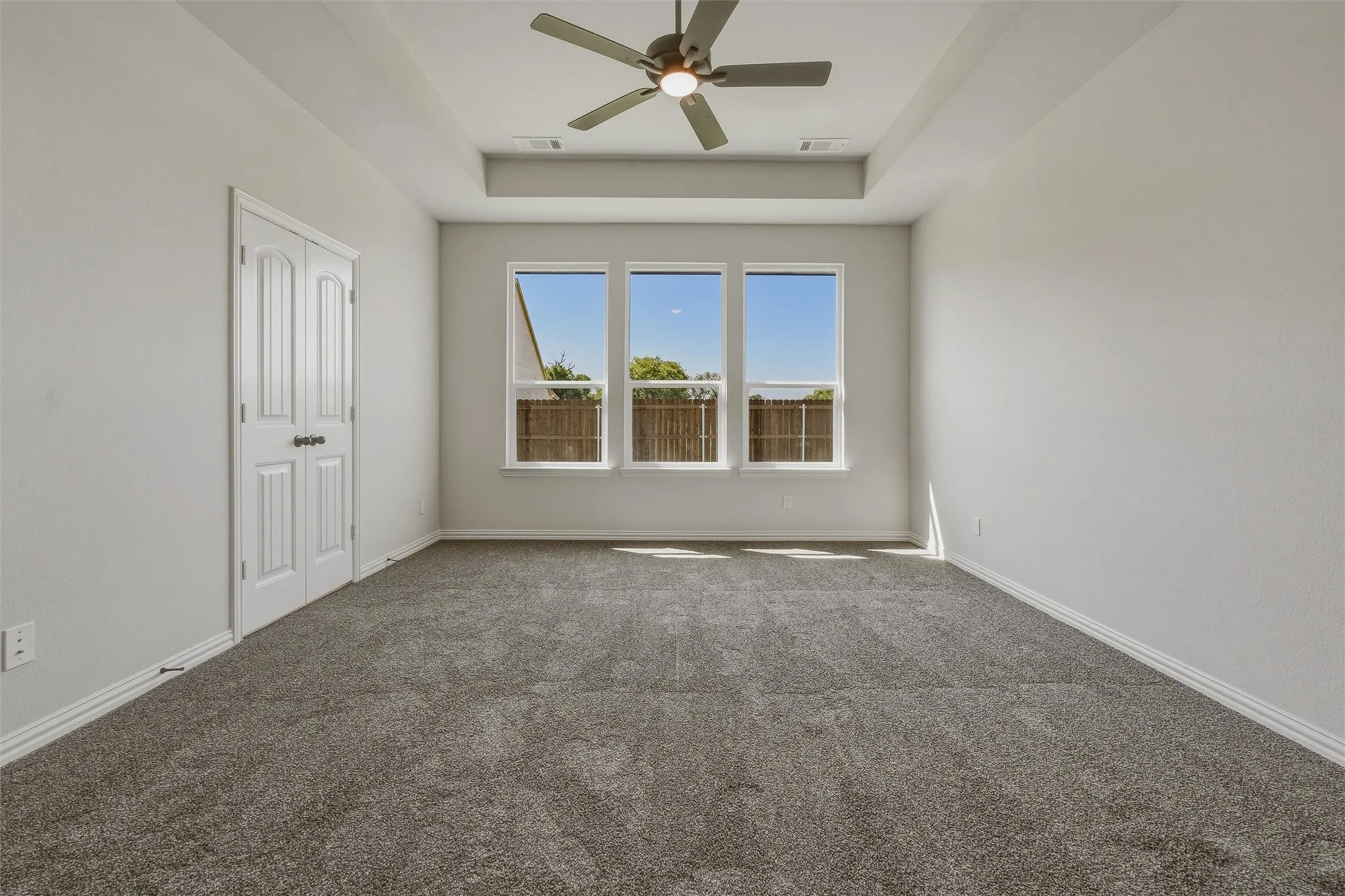 Tray ceiling with a ceiling fan, three pane windows, neutral carpeting, and a double-panel door