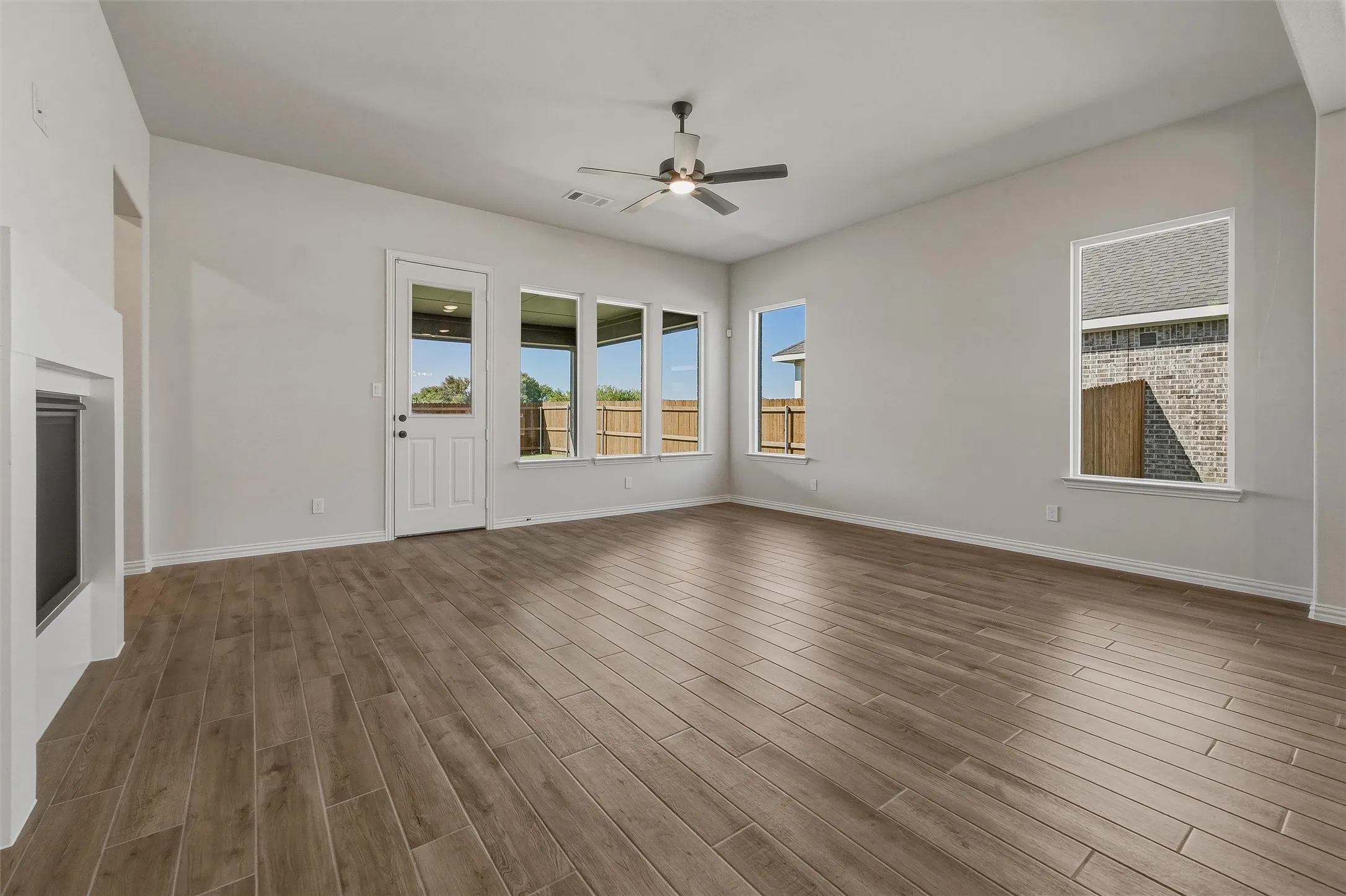 Spacious room featuring wood-finish flooring, multiple windows, a ceiling fan, and a built-in fireplace