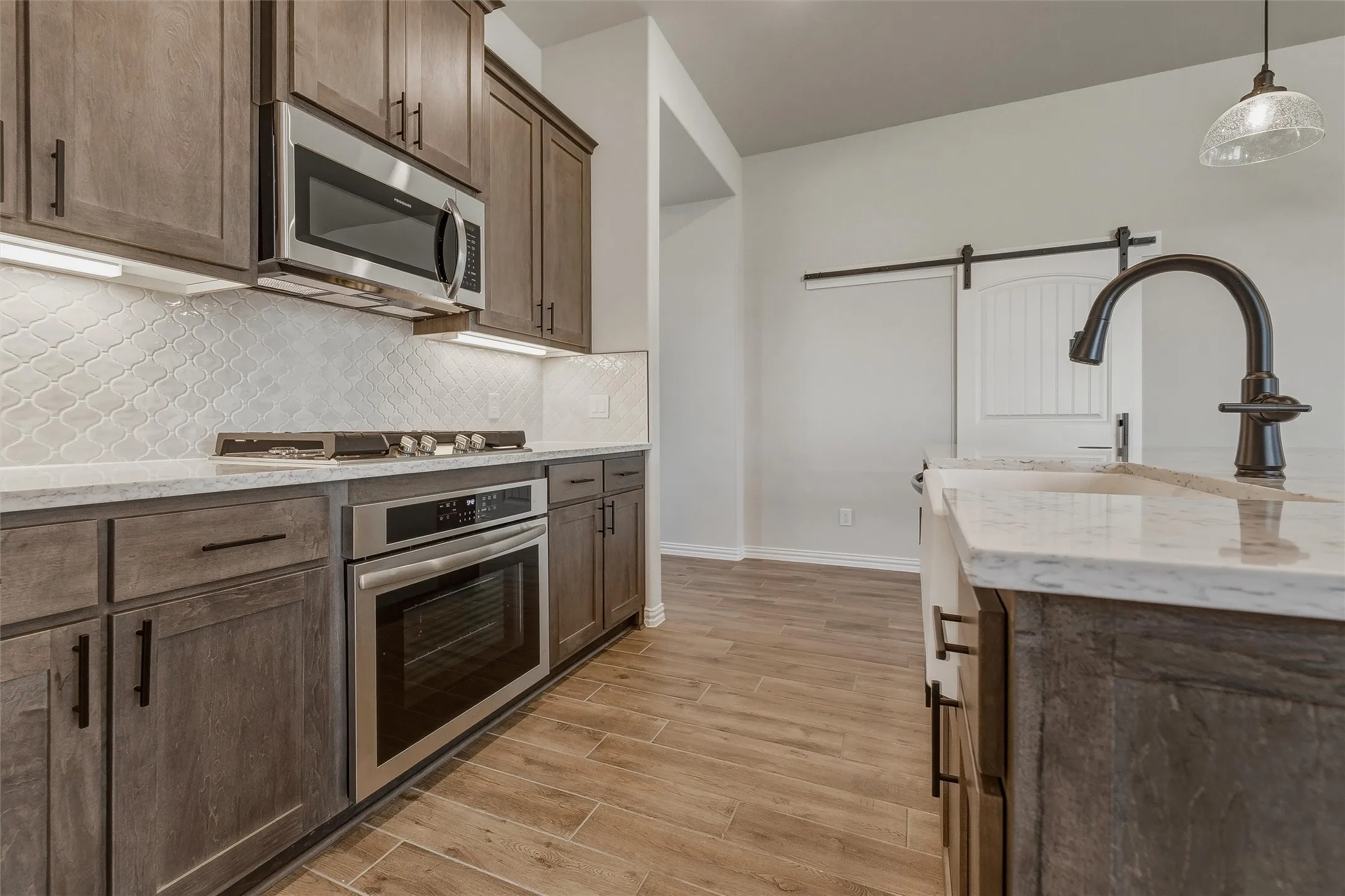 Kitchen featuring wood-finish flooring, stainless steel appliances, white patterned backsplash, and an island with a farmhouse sink