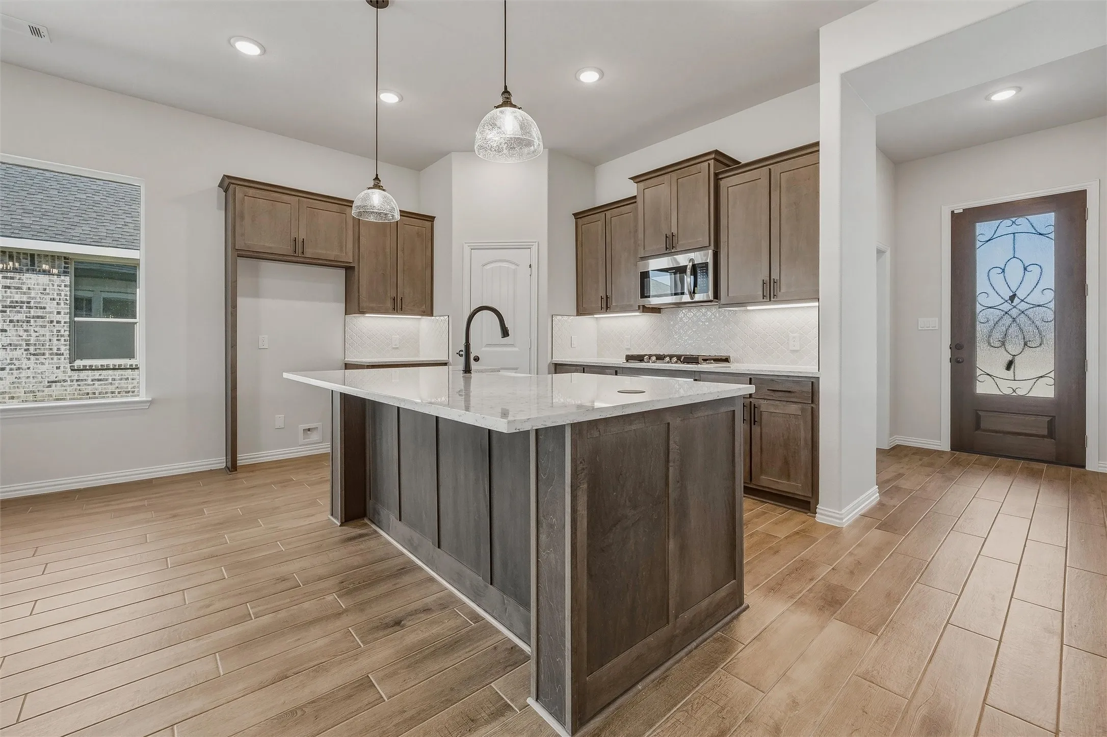 Kitchen with wood-finish flooring, a central island featuring a light-toned countertop, and recessed lighting