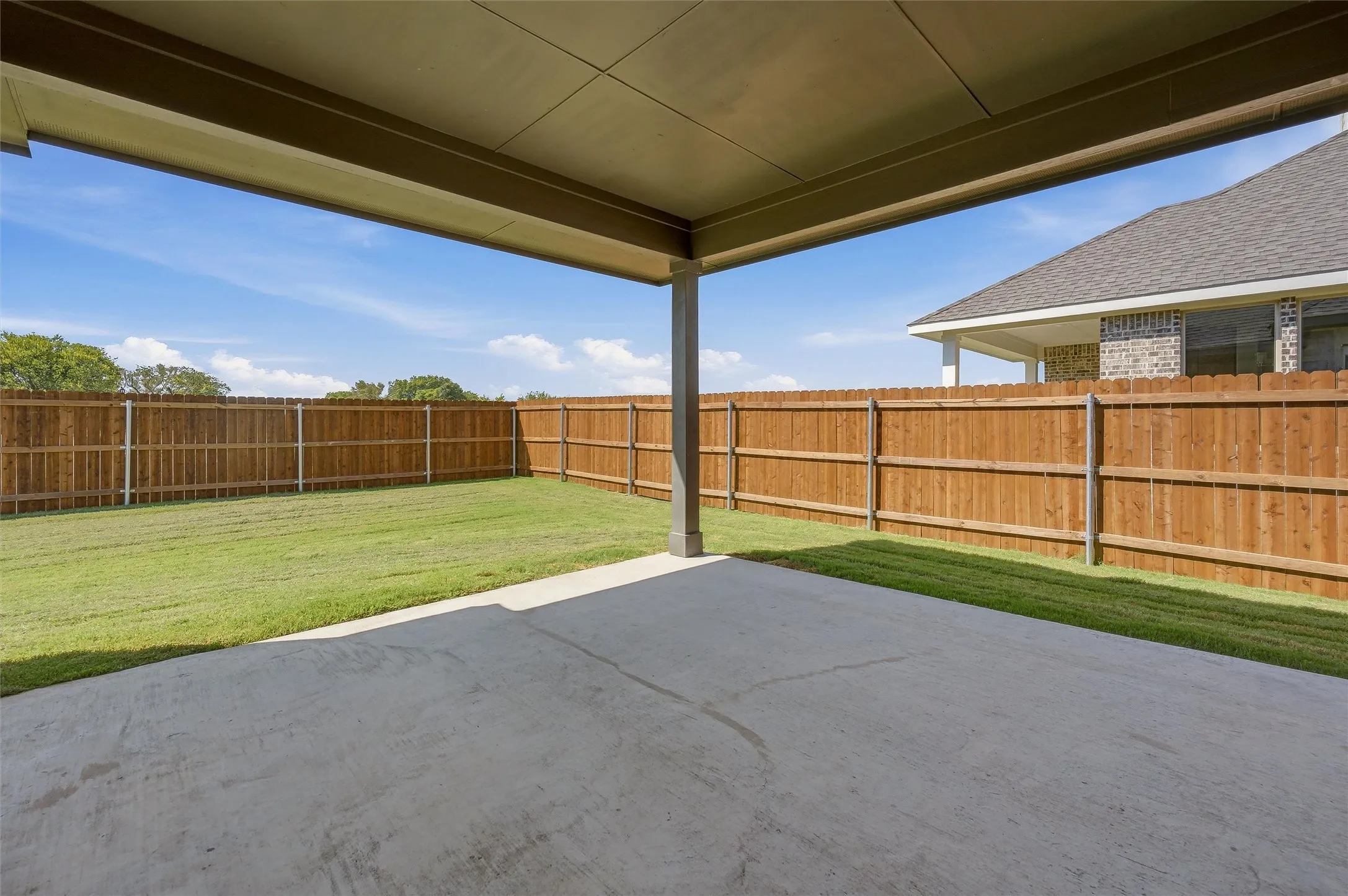 Covered patio with concrete flooring, extending to a fenced backyard with a manicured lawn