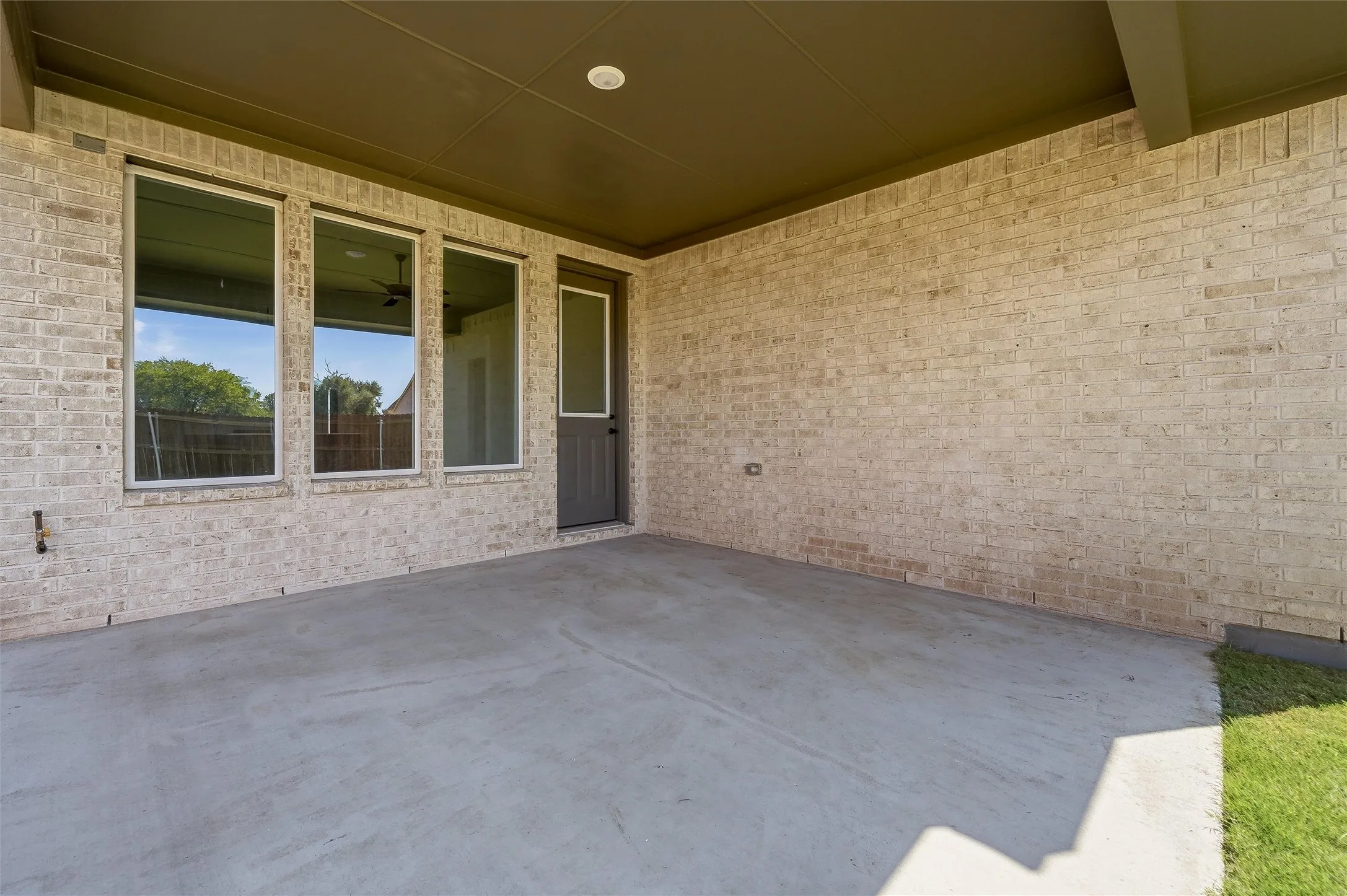 Covered patio with a concrete surface, brick exterior, three large windows, and a side entry door