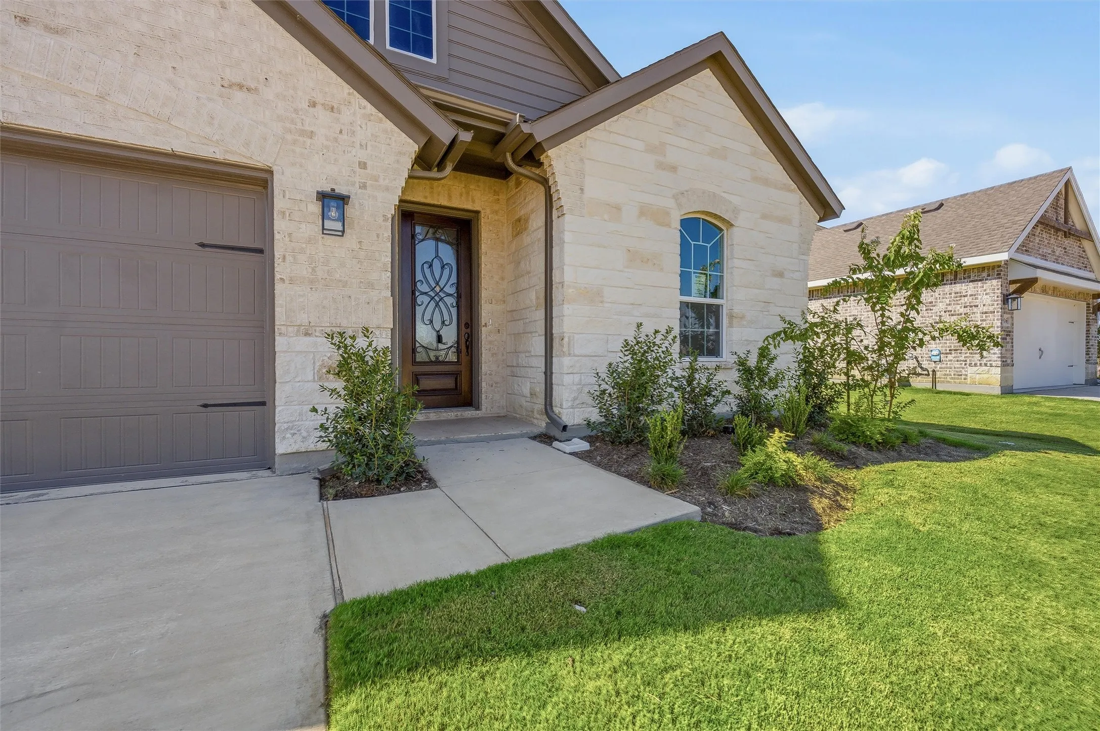 Stone facade home featuring a wood-finish entry door with decorative glass, an arched window, and a paneled garage door