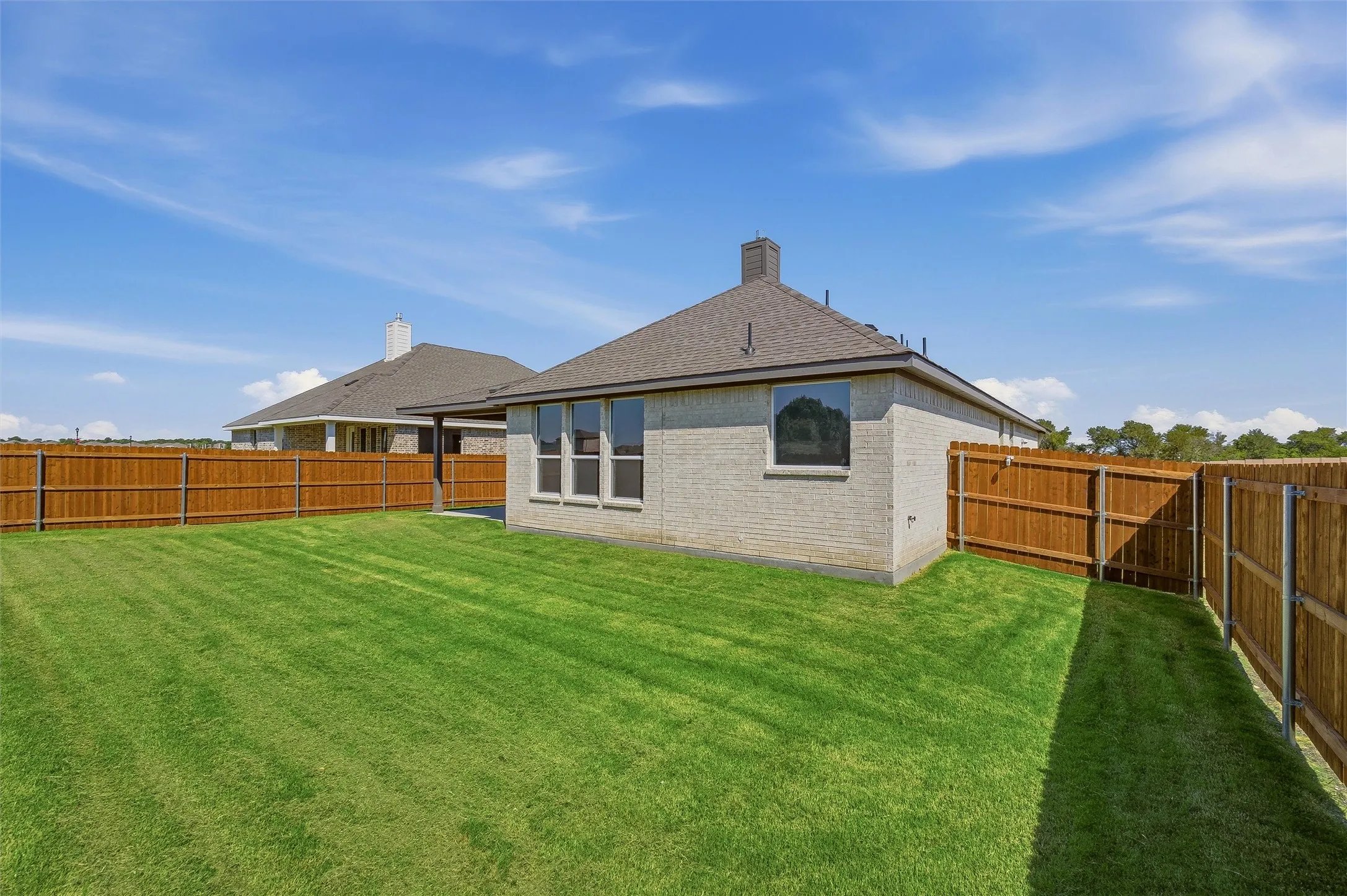 Expansive backyard featuring a manicured lawn, full privacy fencing, and a brick exterior home with a covered patio