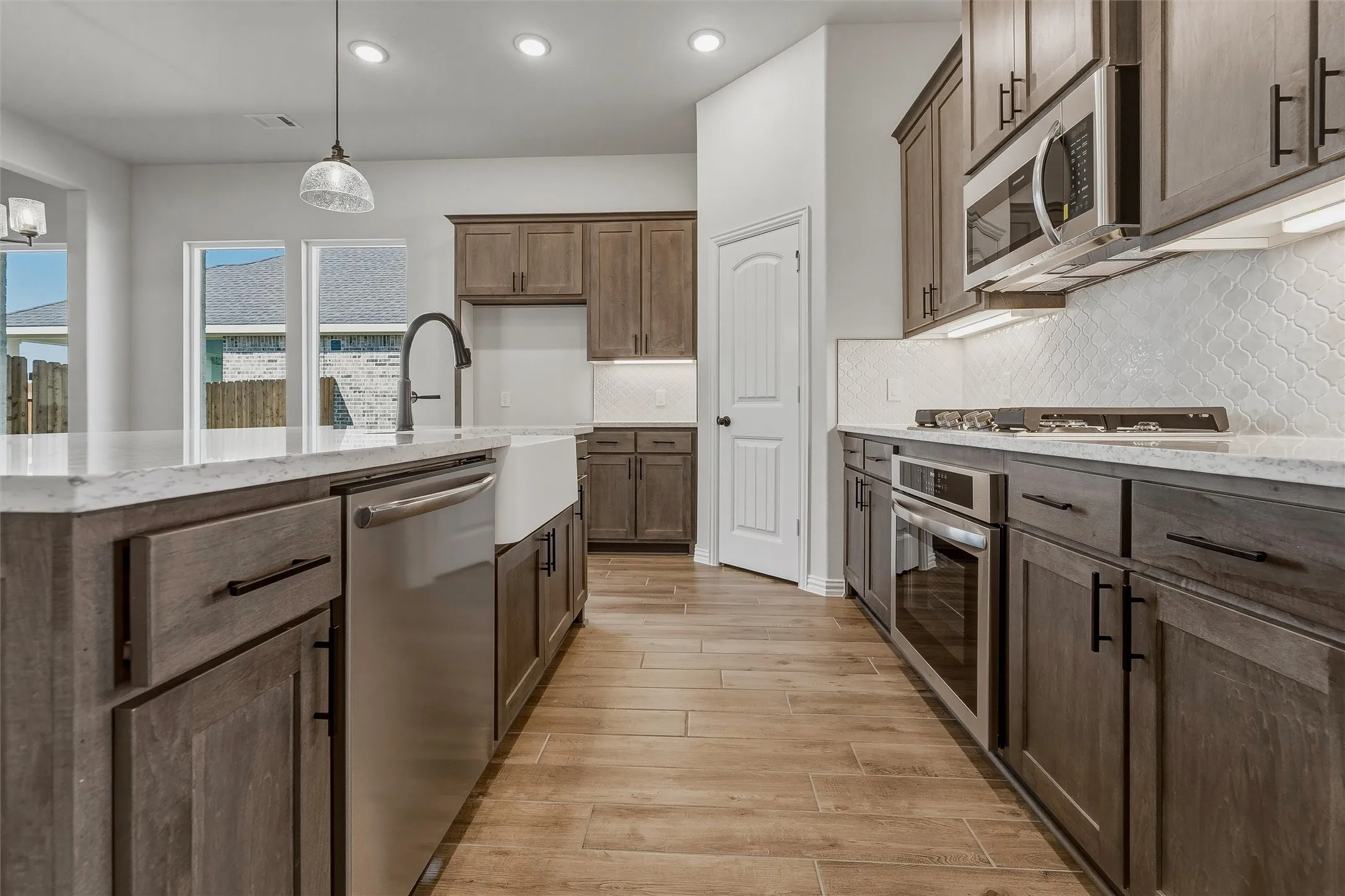 Spacious kitchen with wood-finish flooring, light grey cabinetry, stainless steel appliances, and a farmhouse sink