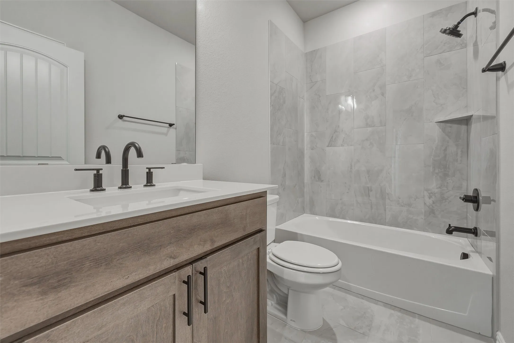 Bathroom featuring a wood-finish vanity with an integrated sink, matte black fixtures, a full-width mirror, and a tiled tub/shower combination with a recessed niche
