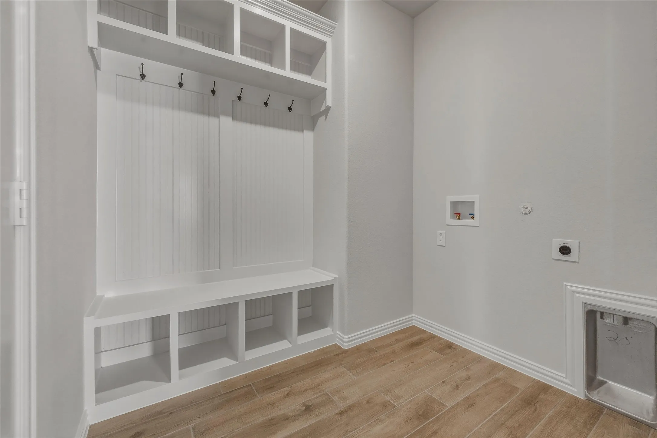 Built-in storage bench with cubbies, upper shelving, coat hooks, and beadboard paneling