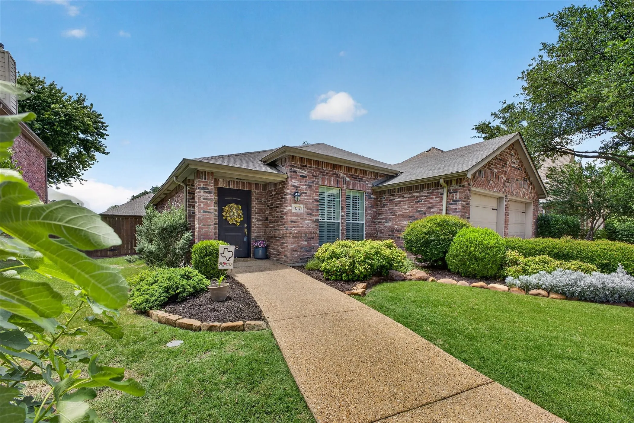Former model home, double garage door, welcoming porch and mature landscaping