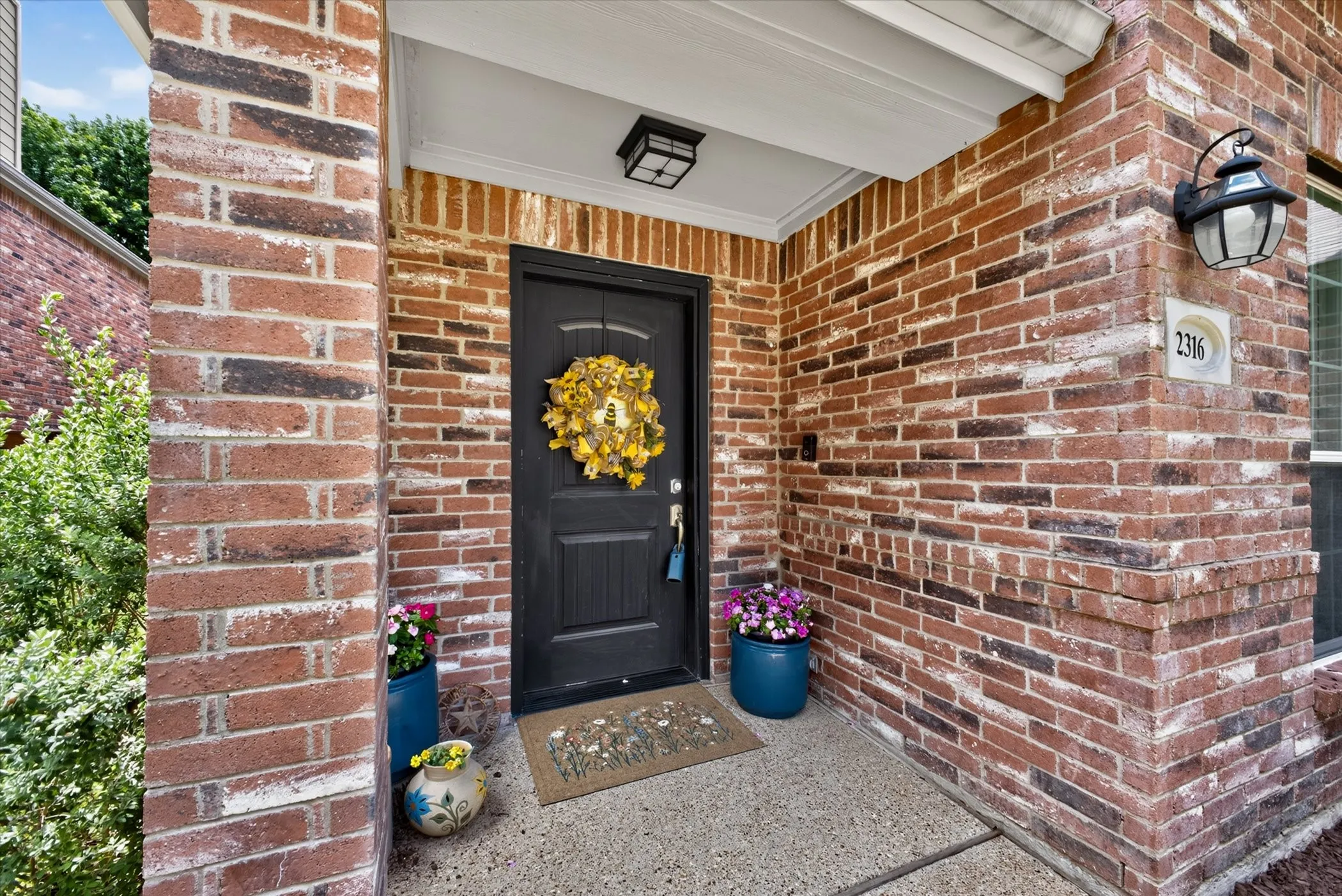 Welcoming covered front porch with exposed aggregate and brick columns