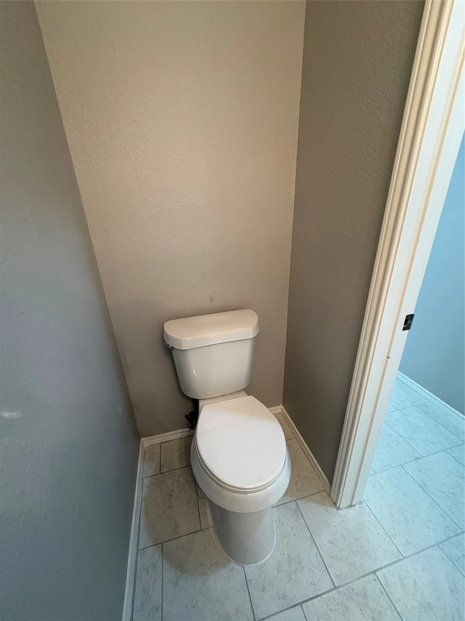 White toilet with light-toned wall finishes and a coordinating tiled floor