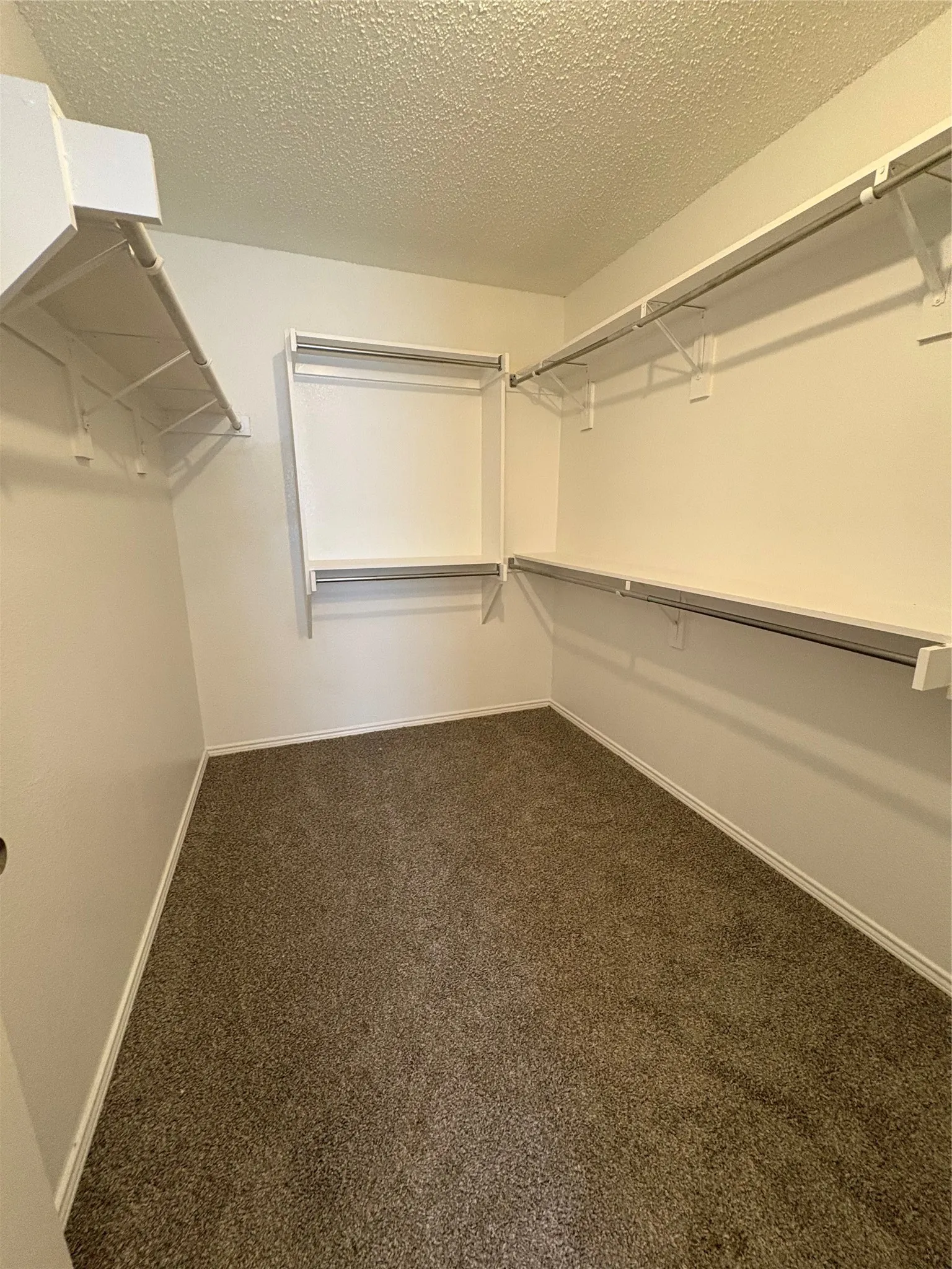 Walk-in closet featuring white wire shelving, multiple hanging rods, and neutral-toned carpet flooring