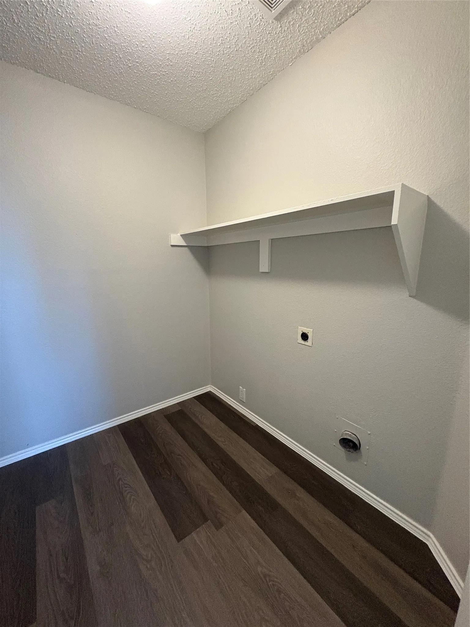 Dedicated utility space featuring wood-finish flooring, white baseboards, and a built-in storage shelf