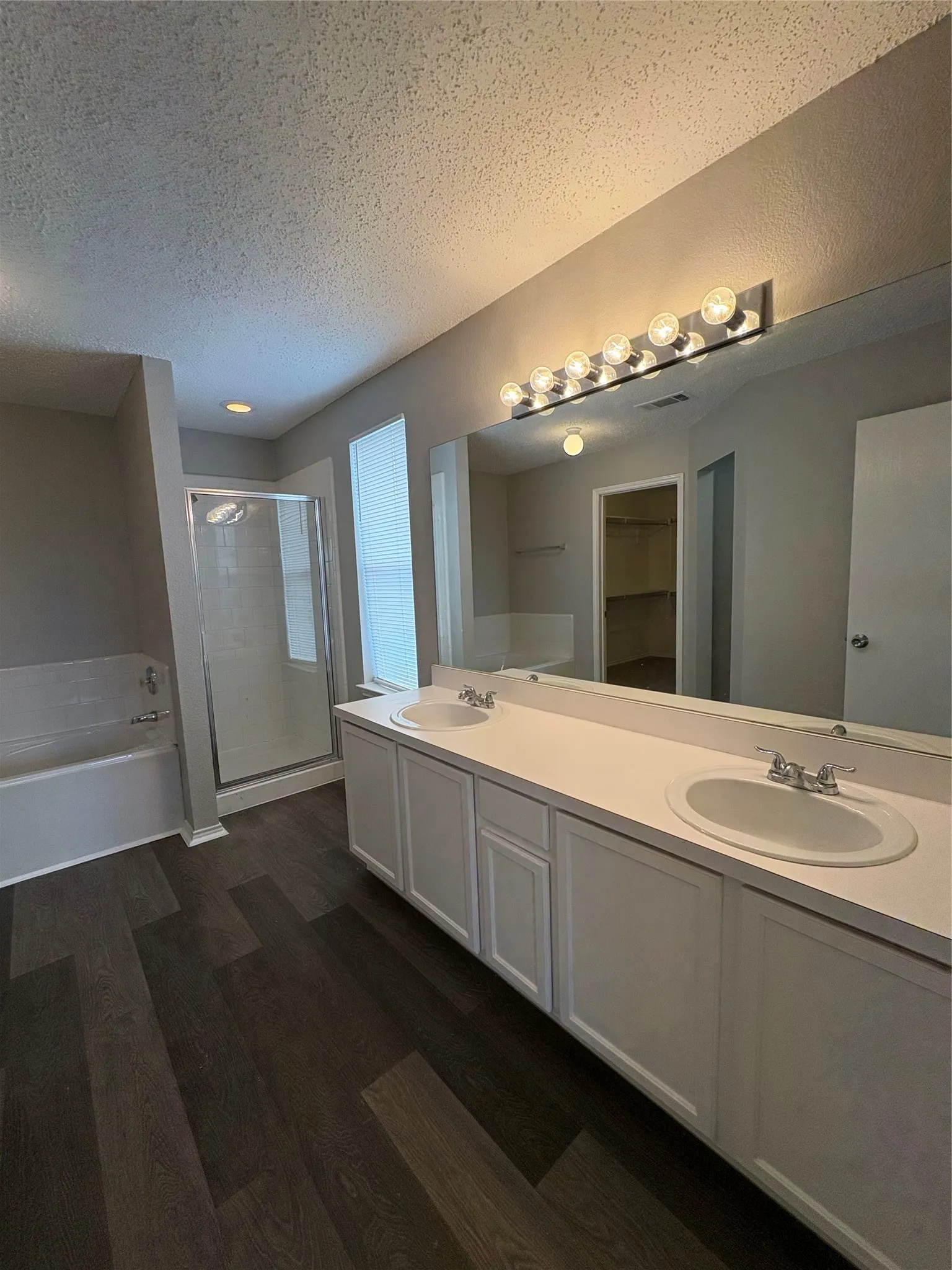 Spacious bathroom featuring a double vanity with white cabinetry and integrated sinks, a large wall-mounted mirror, a separate glass-enclosed shower, and a white soaking tub