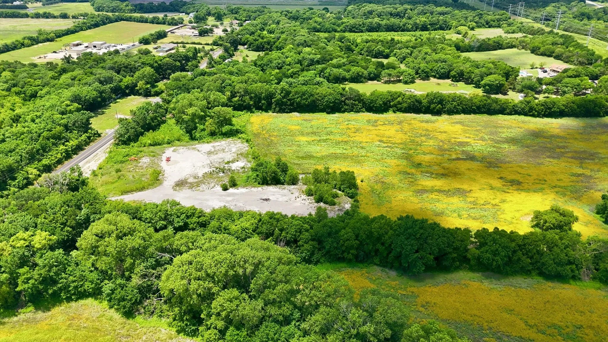Expansive land parcel featuring a gravel-surfaced area, a paved road, and abundant tree coverage