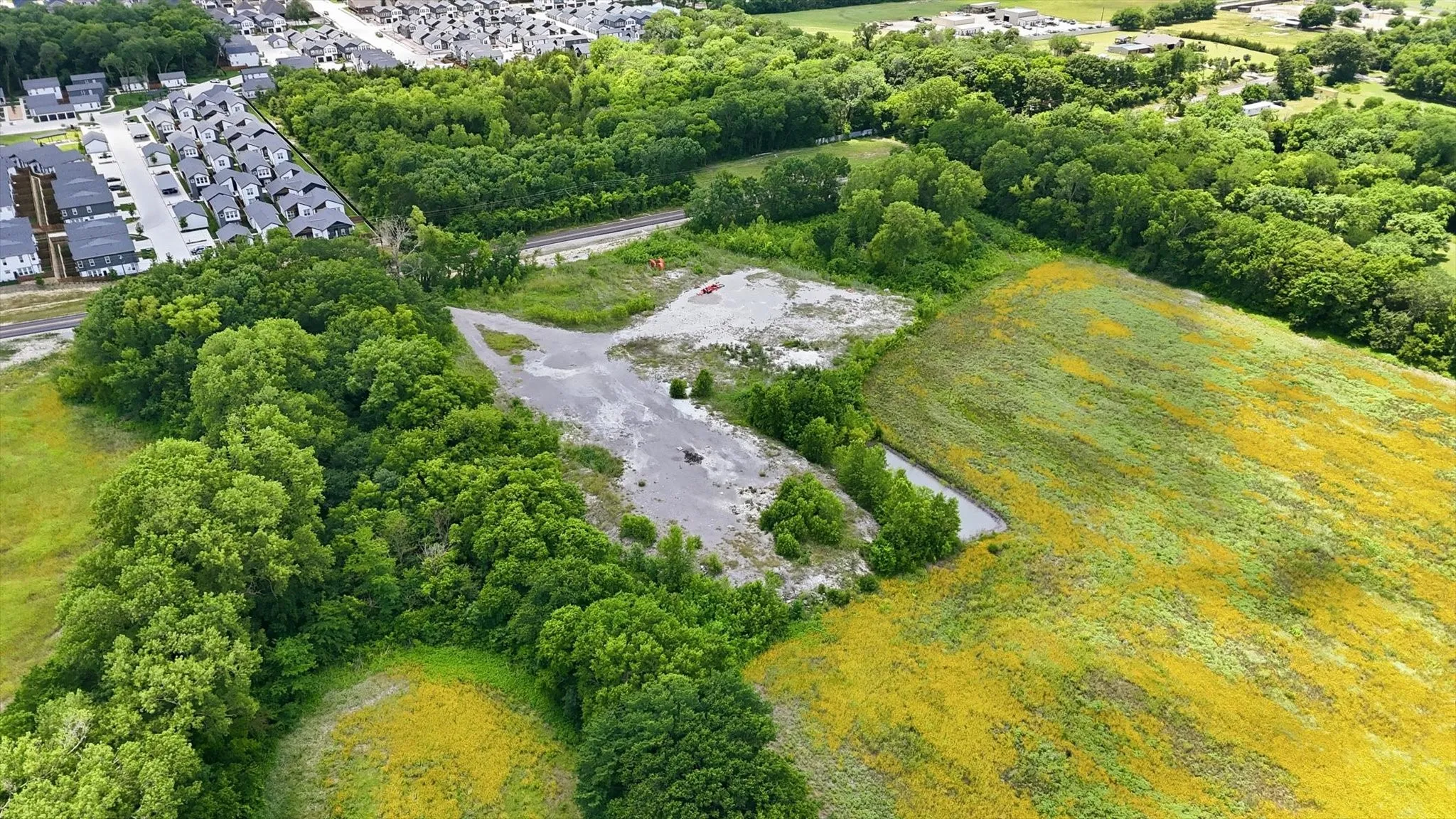 Expansive undeveloped land featuring a mixture of mature trees, open fields, and a gravel access path