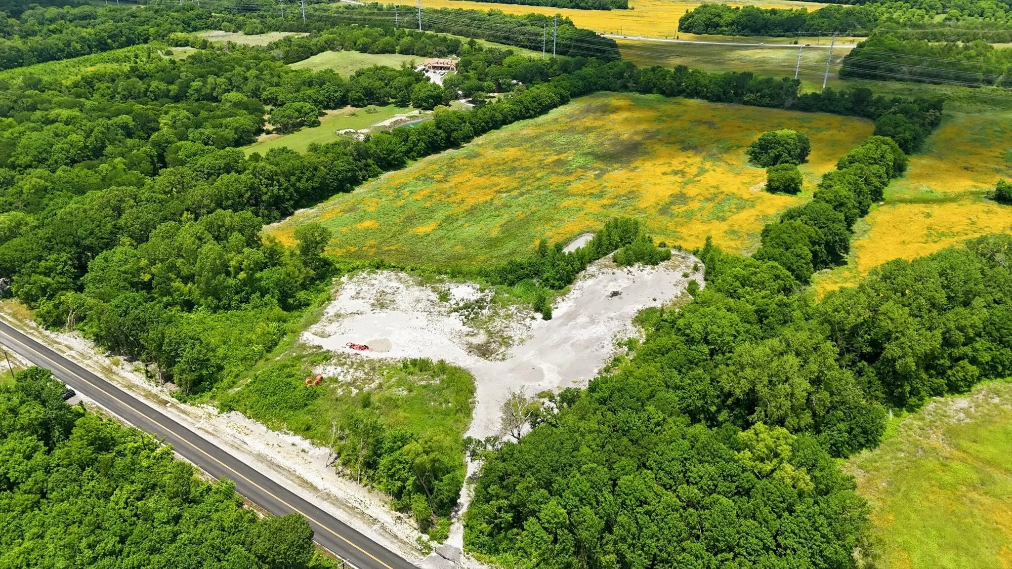 Expansive undeveloped land featuring a paved road frontage, mature tree lines, and a large open field area