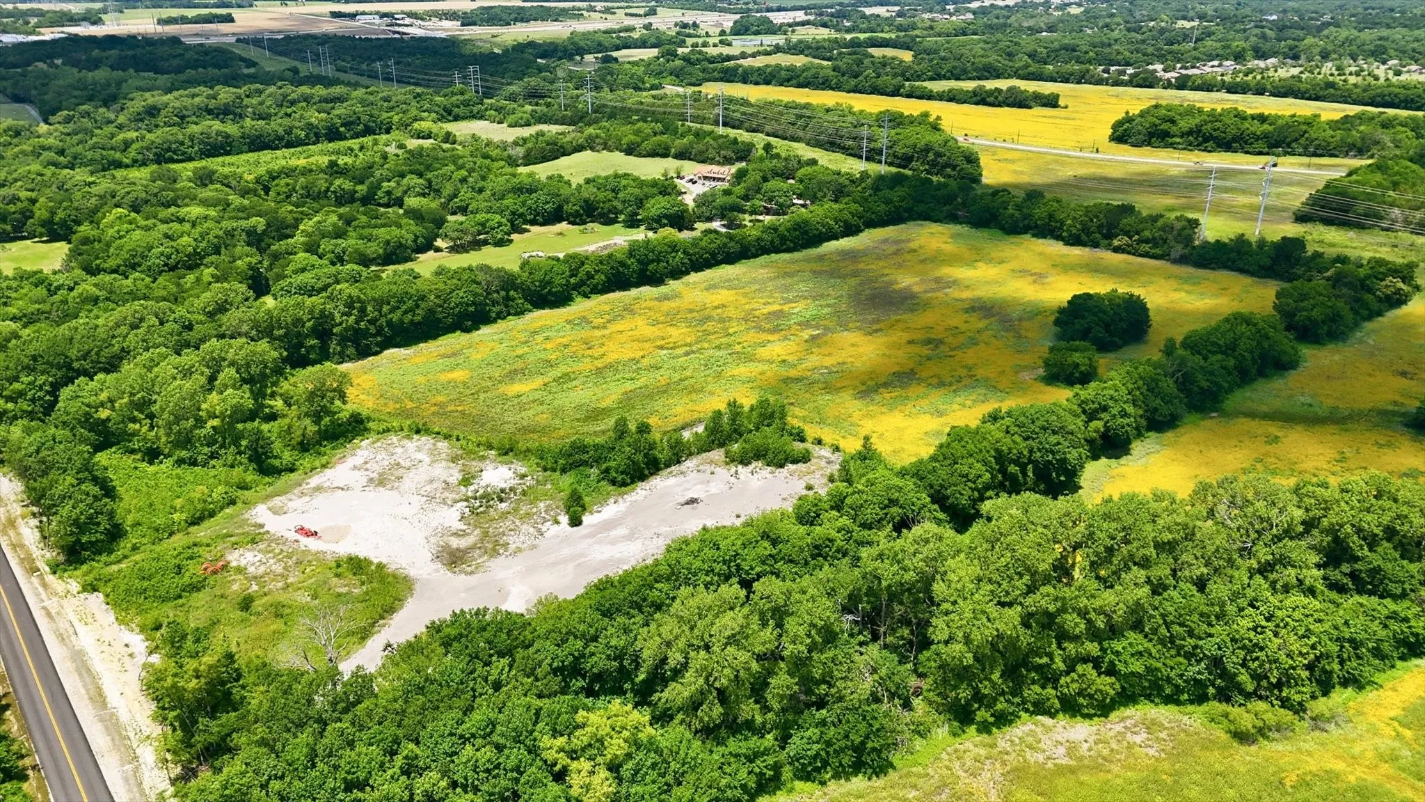 Expansive acreage featuring a partially cleared area, surrounded by mature trees and verdant fields