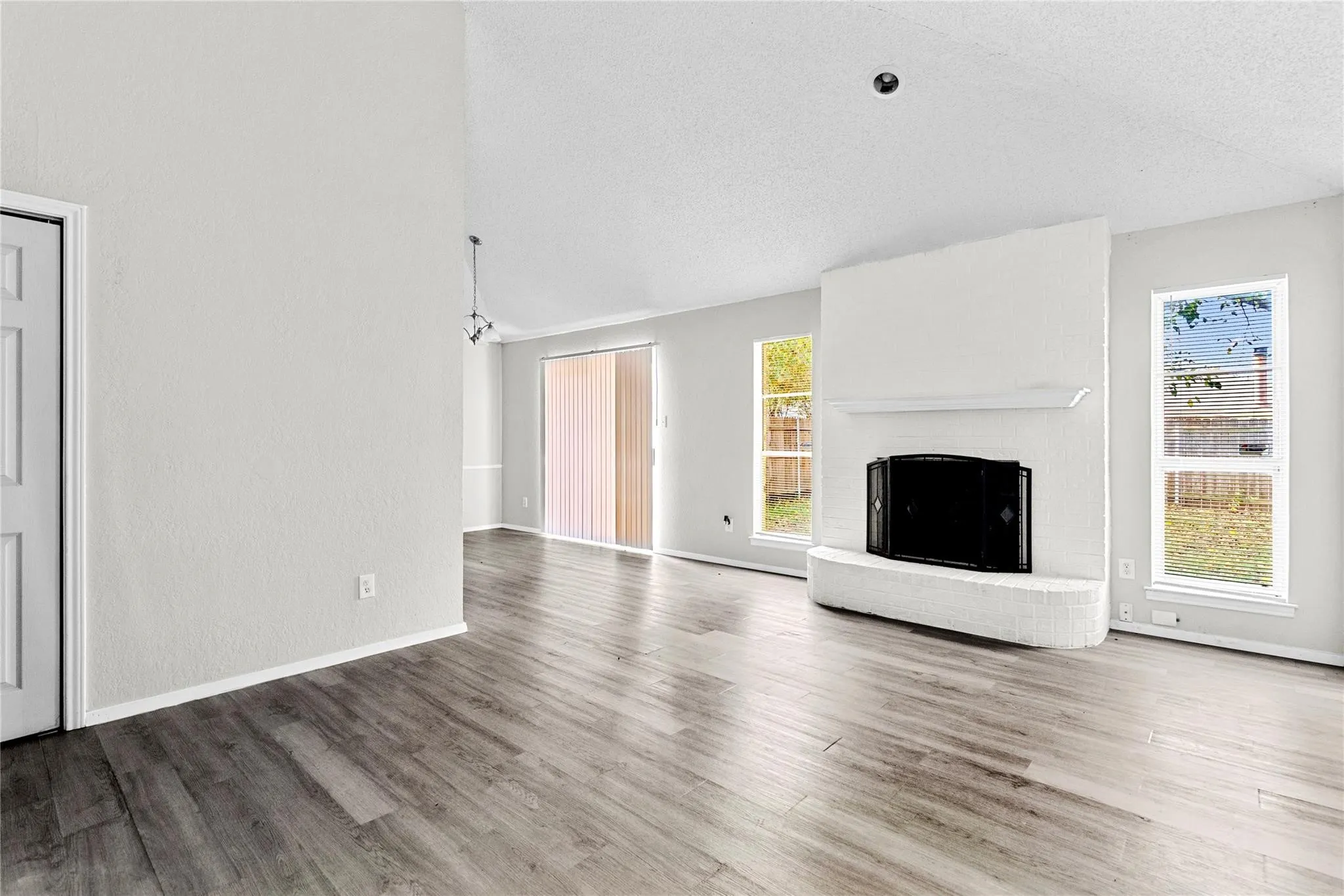 Living area featuring a painted brick fireplace with a mantel, wood-finish flooring, and vaulted ceilings