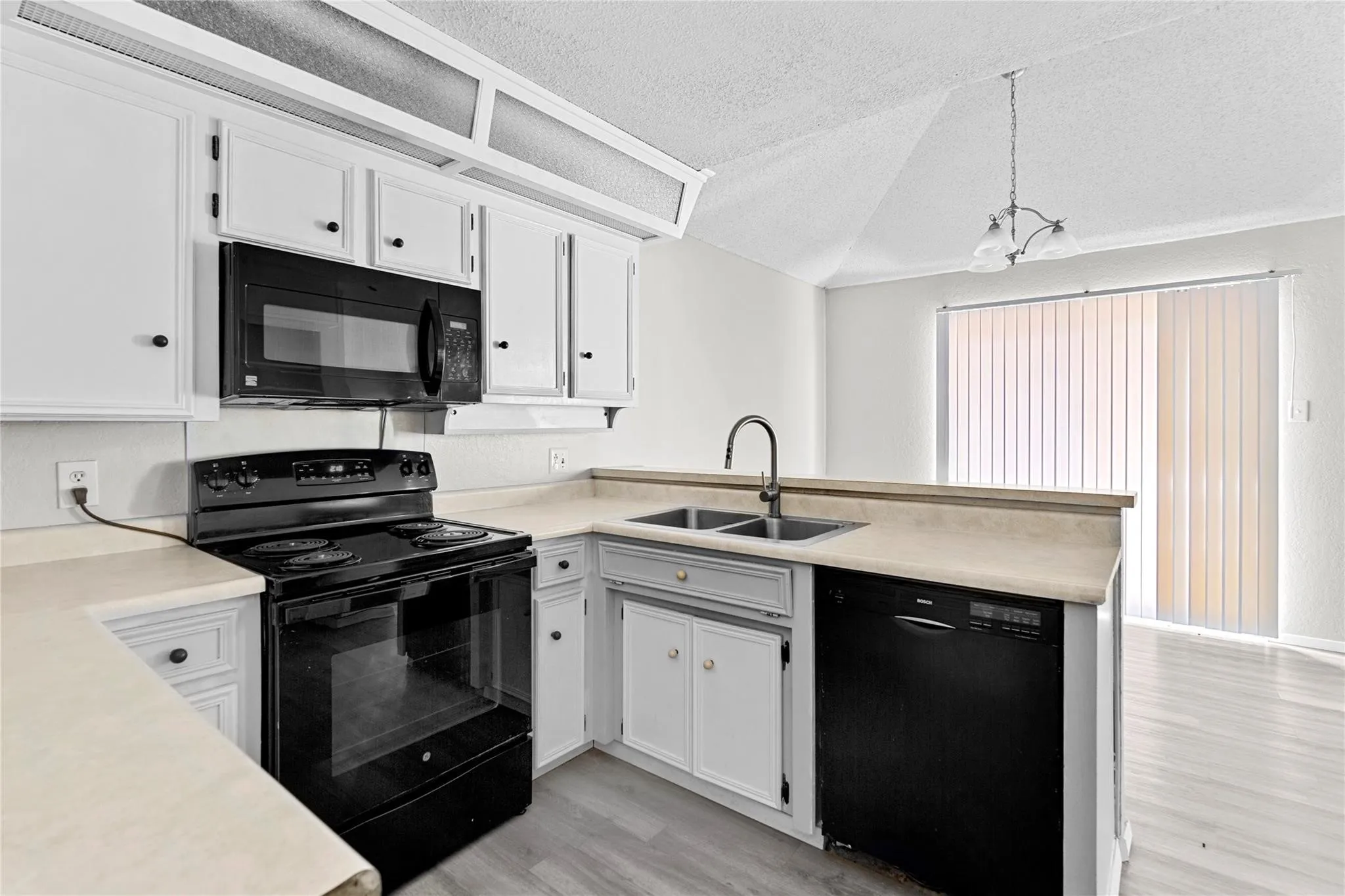 Kitchen featuring white cabinetry with black hardware, an over-the-range microwave, a black electric range, and a double basin sink with a high-arch faucet
