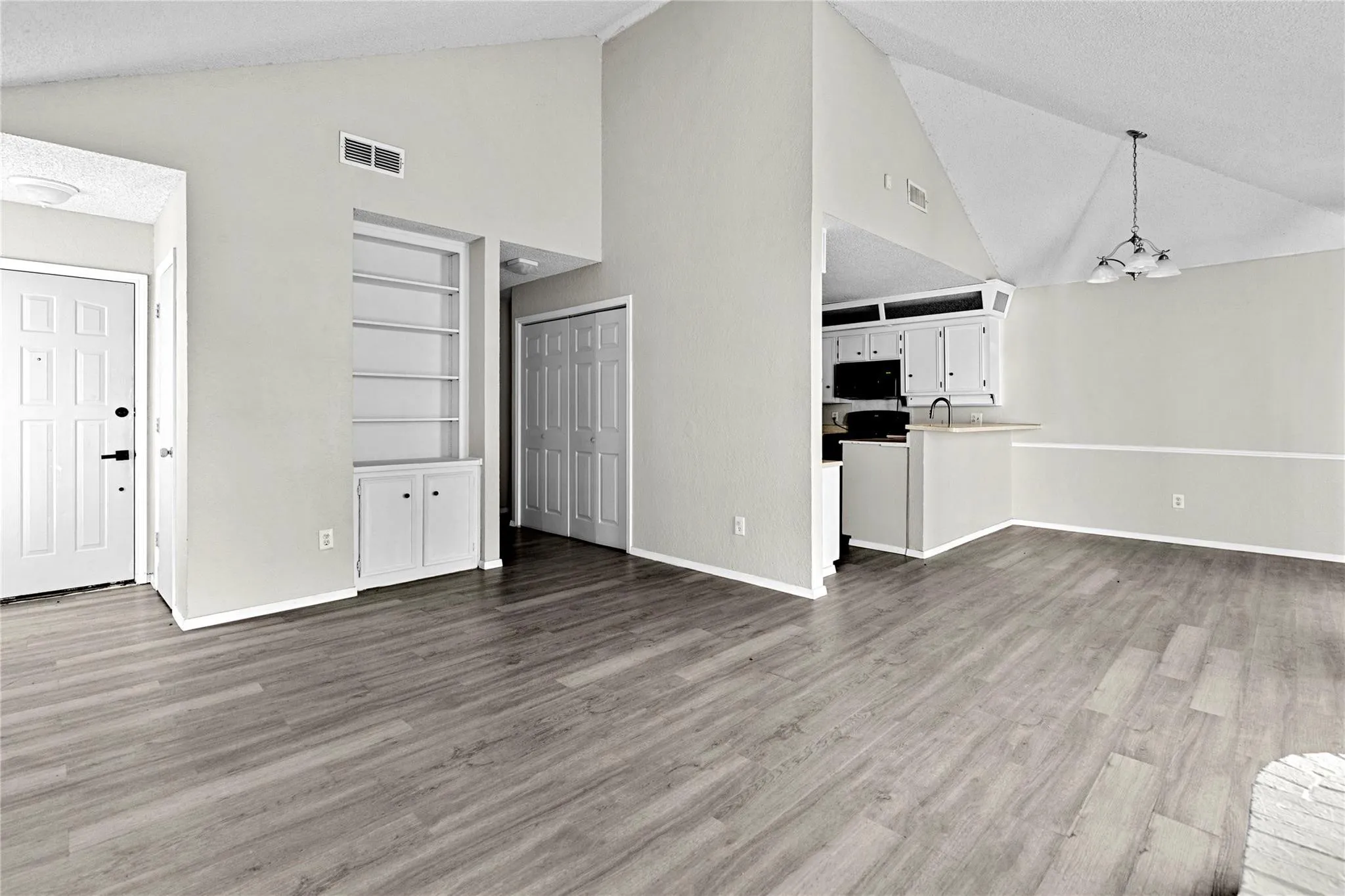 Open concept interior featuring wood-finish flooring, vaulted ceilings, and a built-in bookshelf with cabinet storage