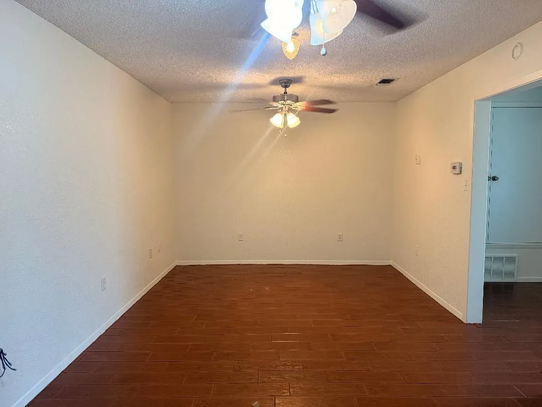 Spacious room featuring wood-finish flooring, white walls, and dual ceiling fans with integrated lighting
