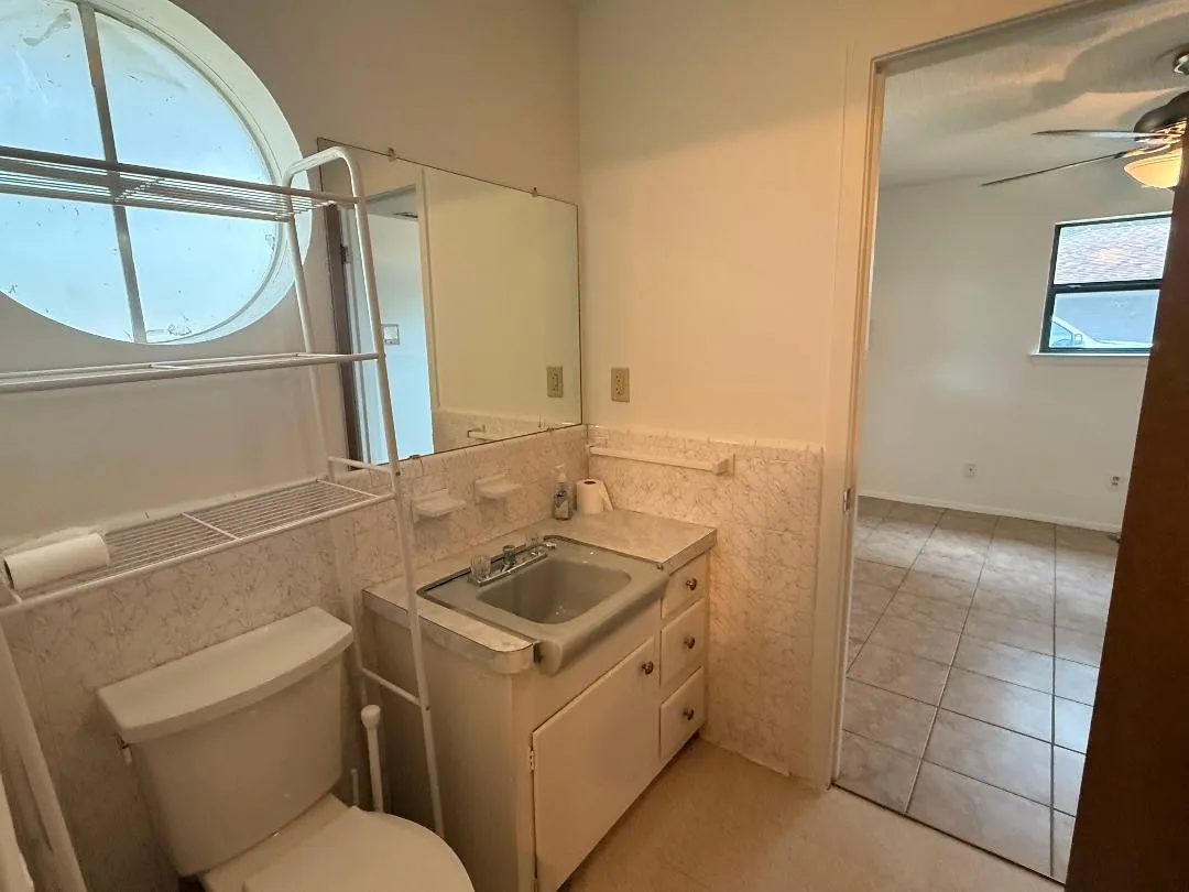 Bathroom featuring a circular window, tiled walls, a vanity with an integrated sink, and a commode