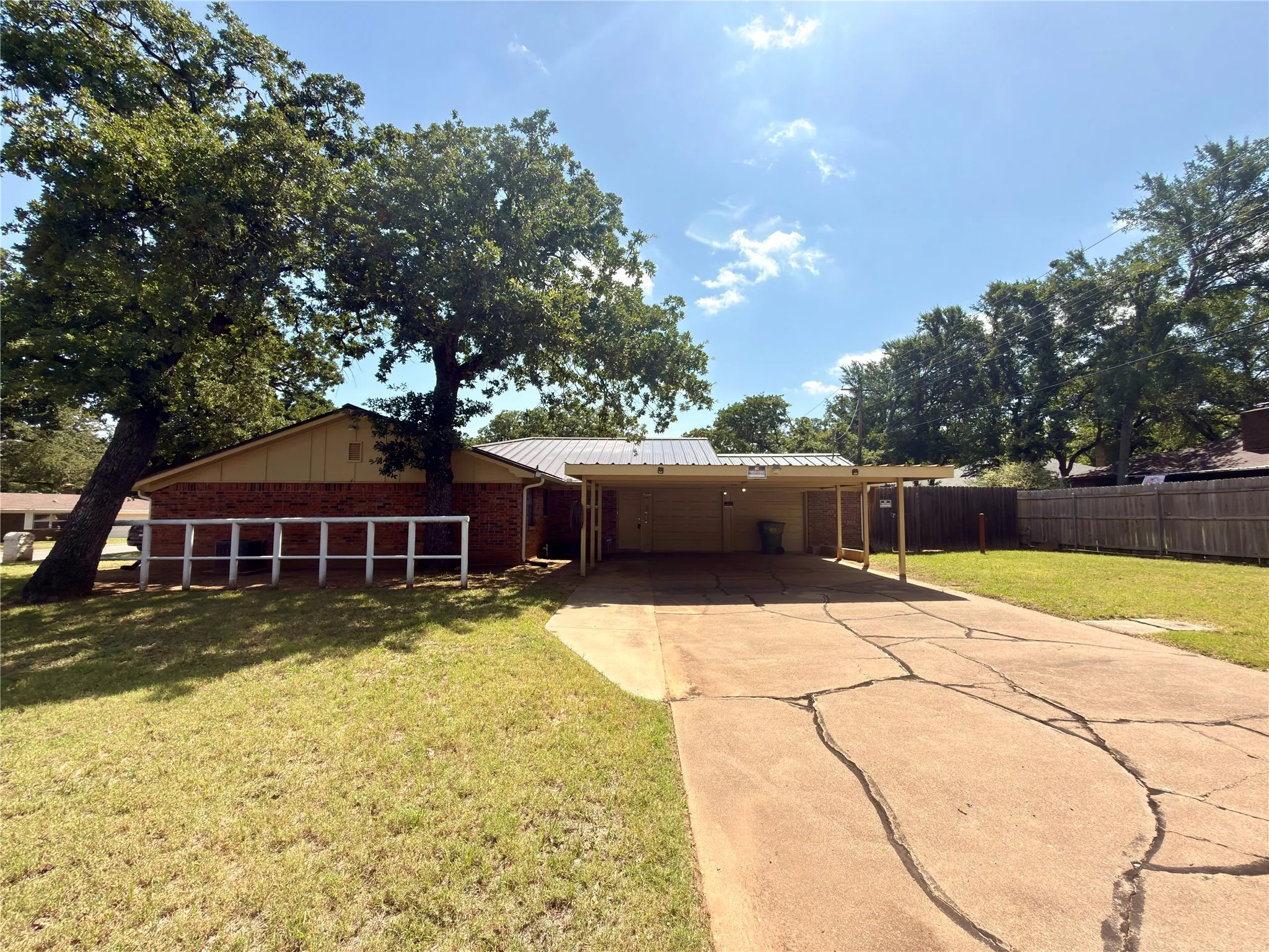 Brick exterior with a metal roof, featuring a covered carport and a spacious front lawn