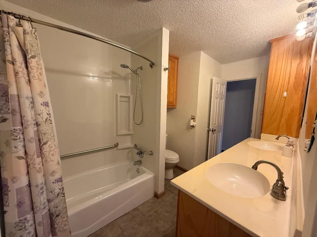 Full bathroom featuring a white tub/shower combination with grab bars, a dual-sink vanity with light-colored countertops, and wood-finish cabinetry