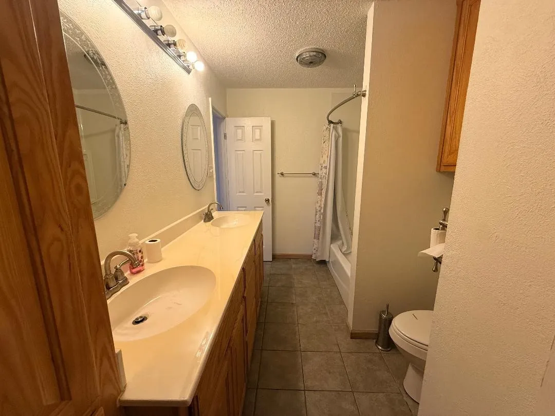 Dual vanity with integrated sinks, wood-finish cabinetry, and contemporary lighting fixtures