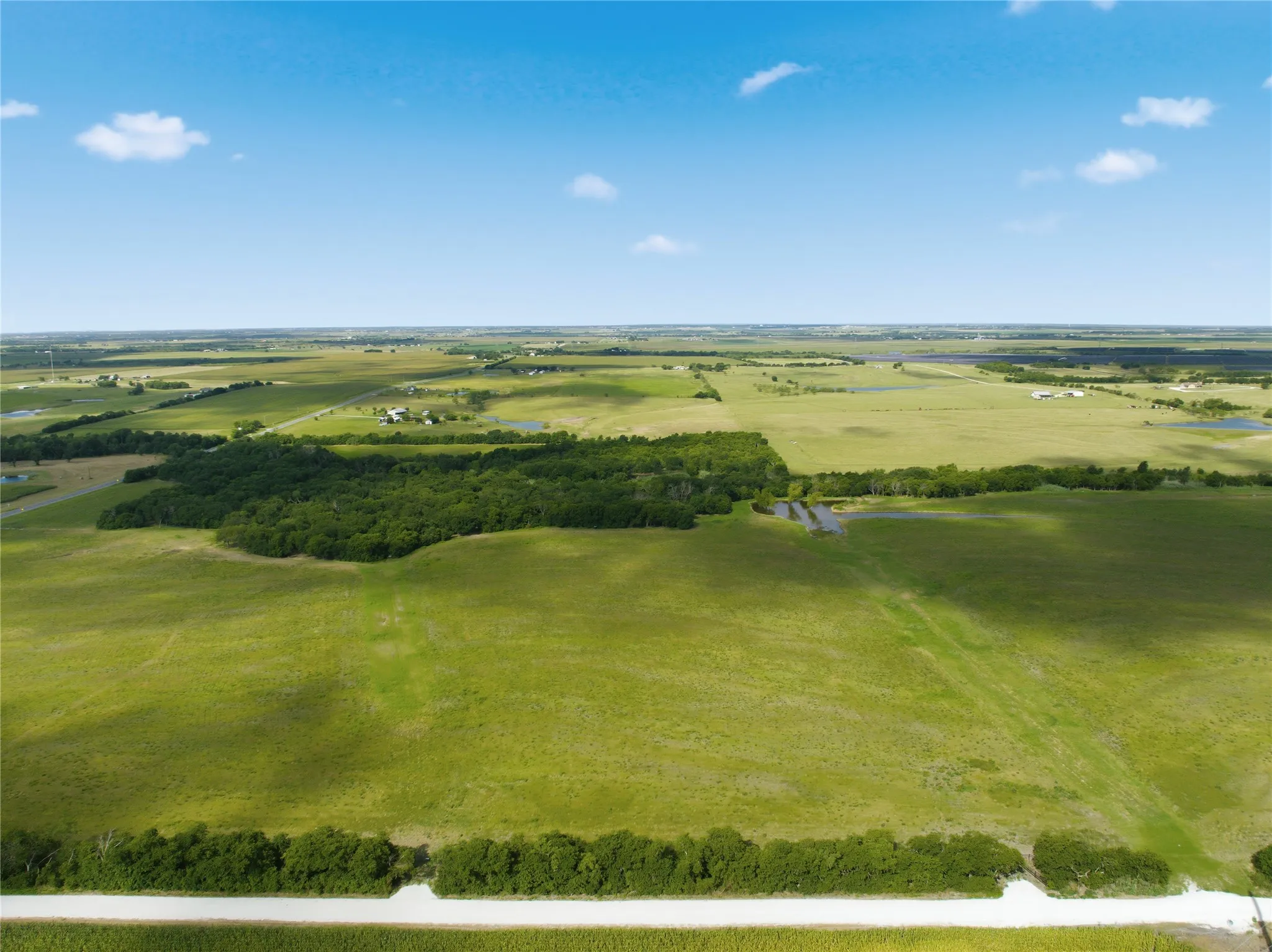 Expansive rural landscape featuring vast green fields, tree lines, and multiple ponds