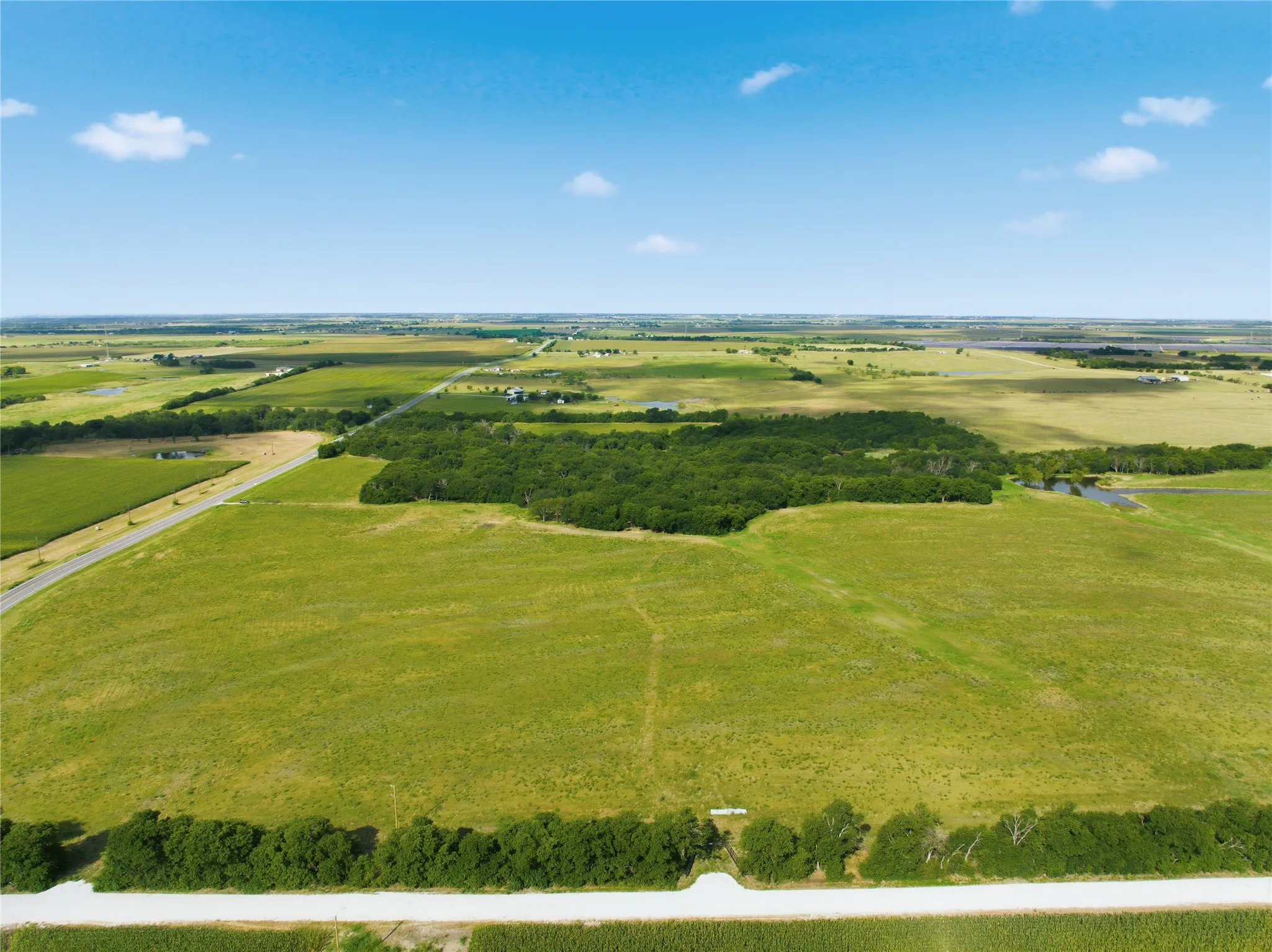 Expansive green fields with a central treeline and distant bodies of water