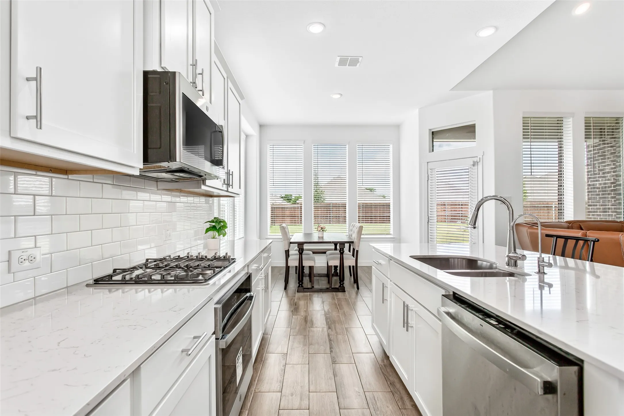 Kitchen featuring white cabinetry, subway tile backsplash, stainless steel appliances, wood-finish flooring, and white countertops