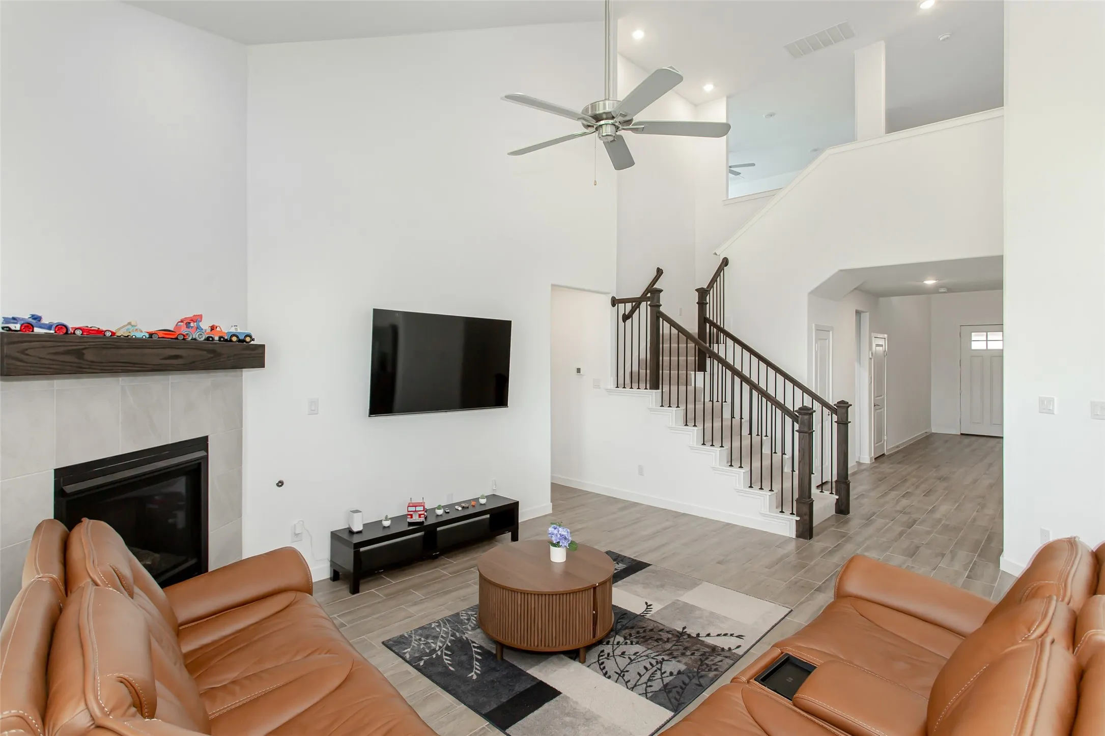 Two-story living area featuring a fireplace with a wood mantel, a ceiling fan, a staircase with dark wood newel posts and metal balusters, and wood-finish flooring