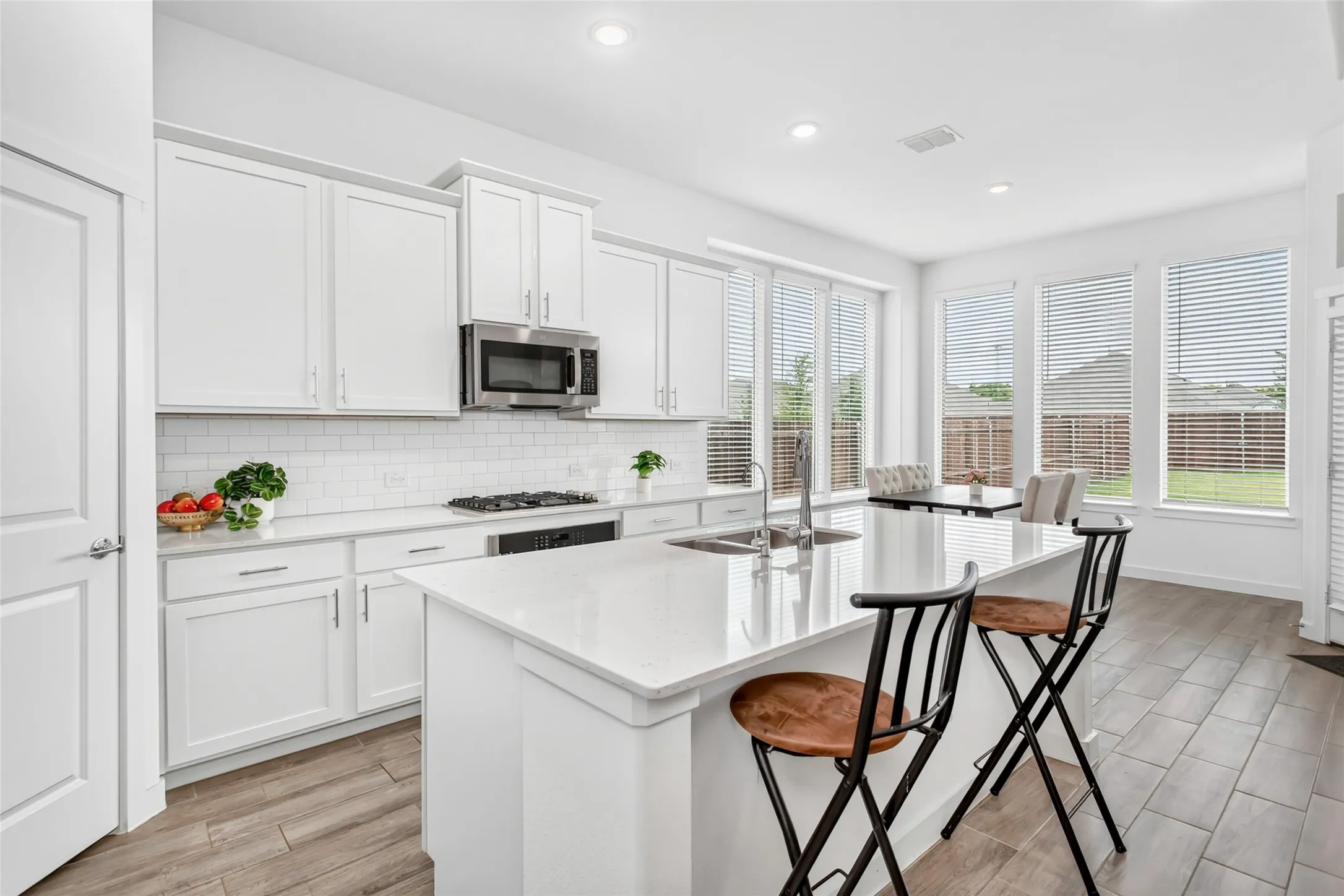 Contemporary kitchen featuring an island with a stainless steel sink, white cabinetry, a subway tile backsplash, stainless steel appliances, and wood-finish flooring