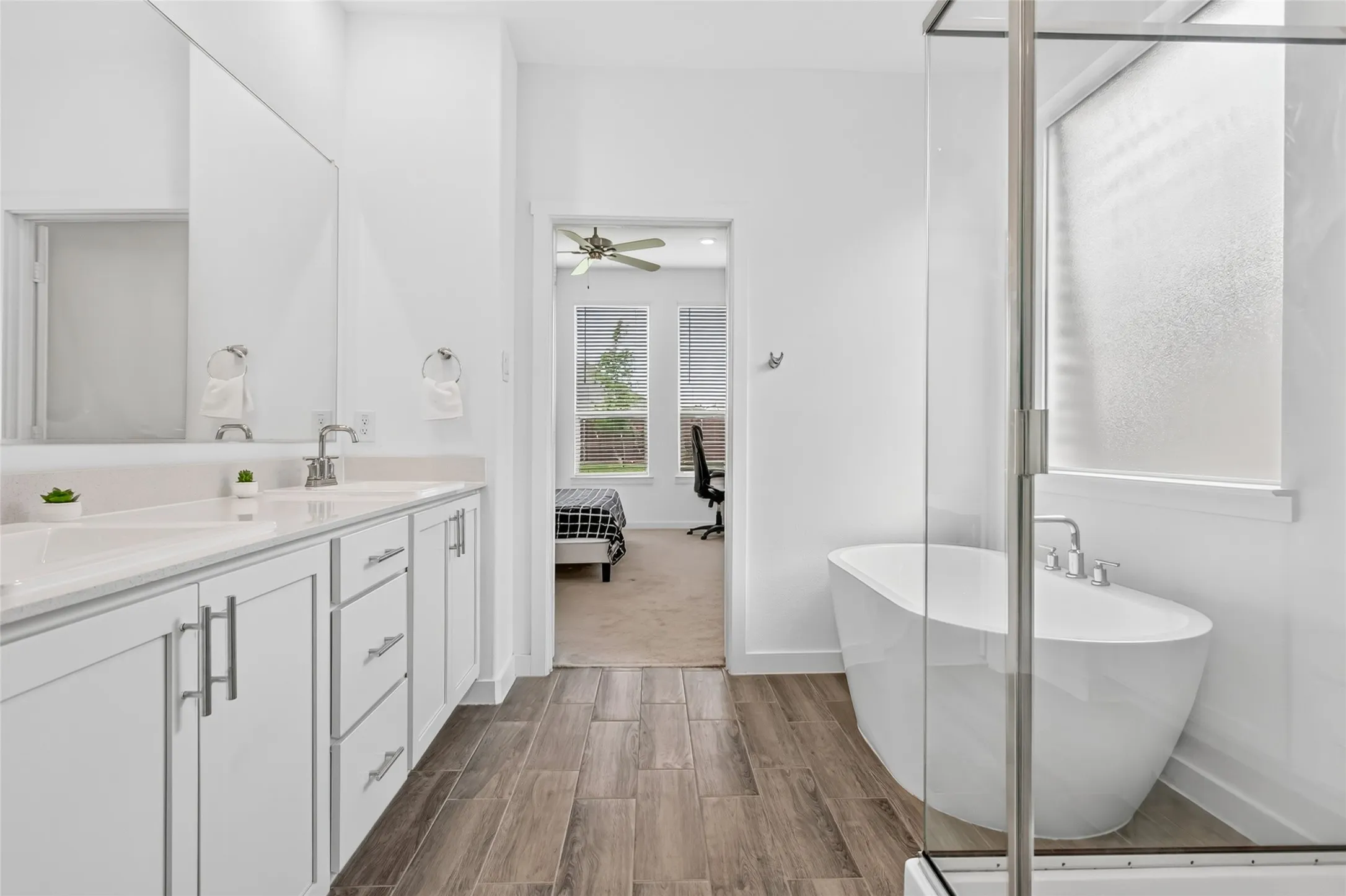Spacious bathroom featuring a freestanding soaking tub, walk-in shower with glass enclosure, dual vanity with undermount sinks, and wood-finish flooring